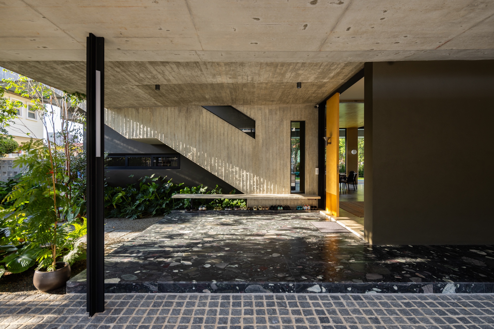 Black steel staircase against a board-formed concrete wall with dappled sunlight from overhead openings