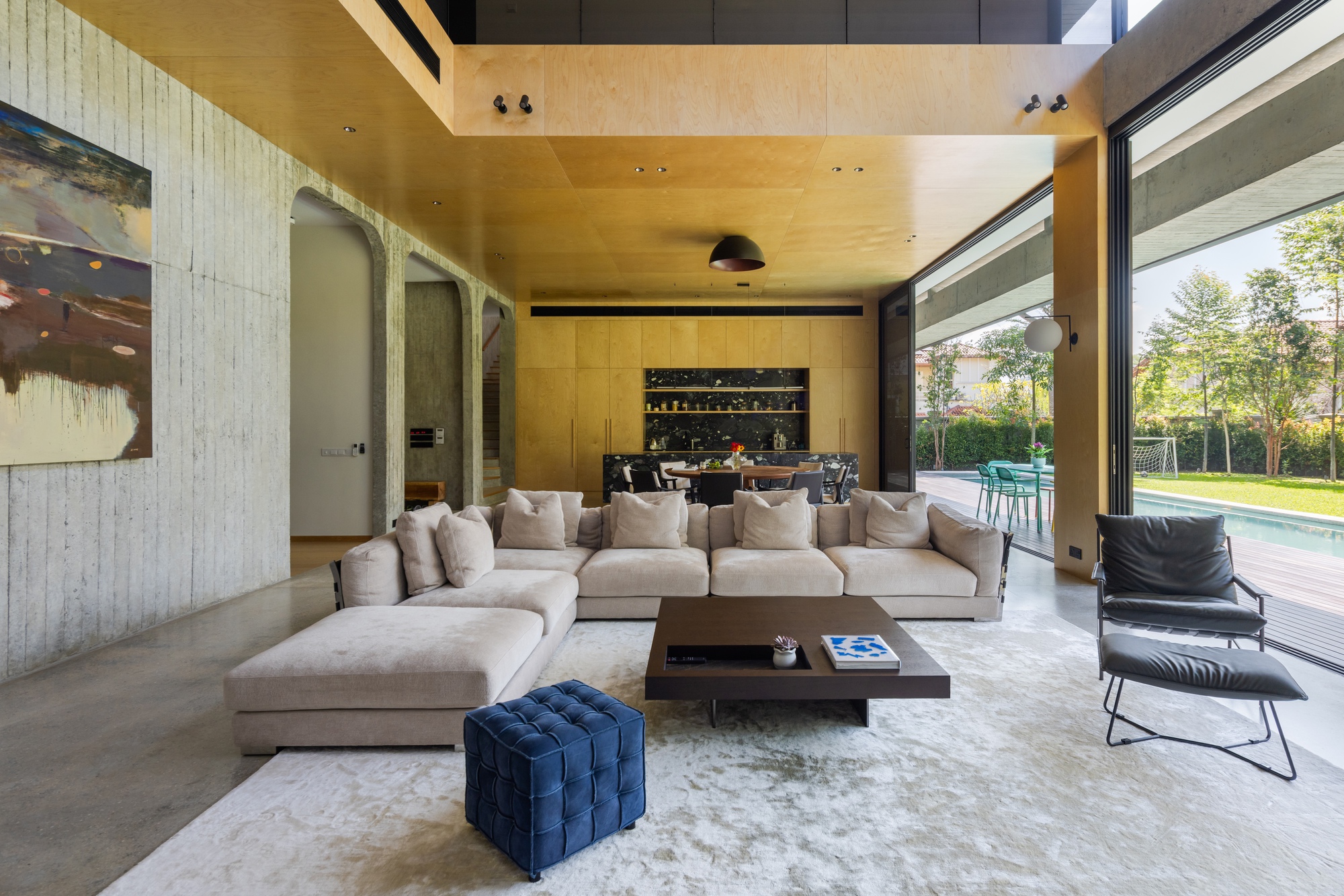 Living room with plywood ceiling and cabinetry opening to lawn and trees through sliding glass doors