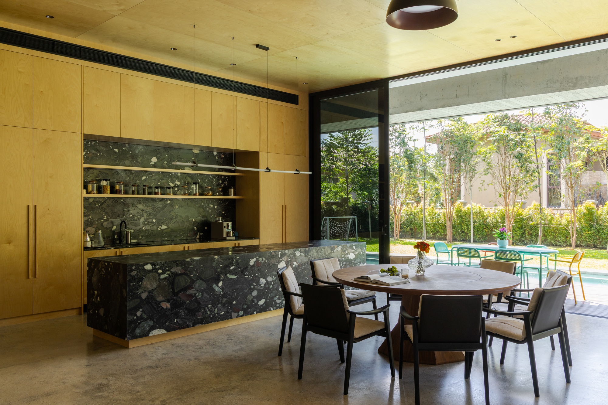Kitchen and dining area with terrazzo island and plywood cabinetry opening to a garden courtyard
