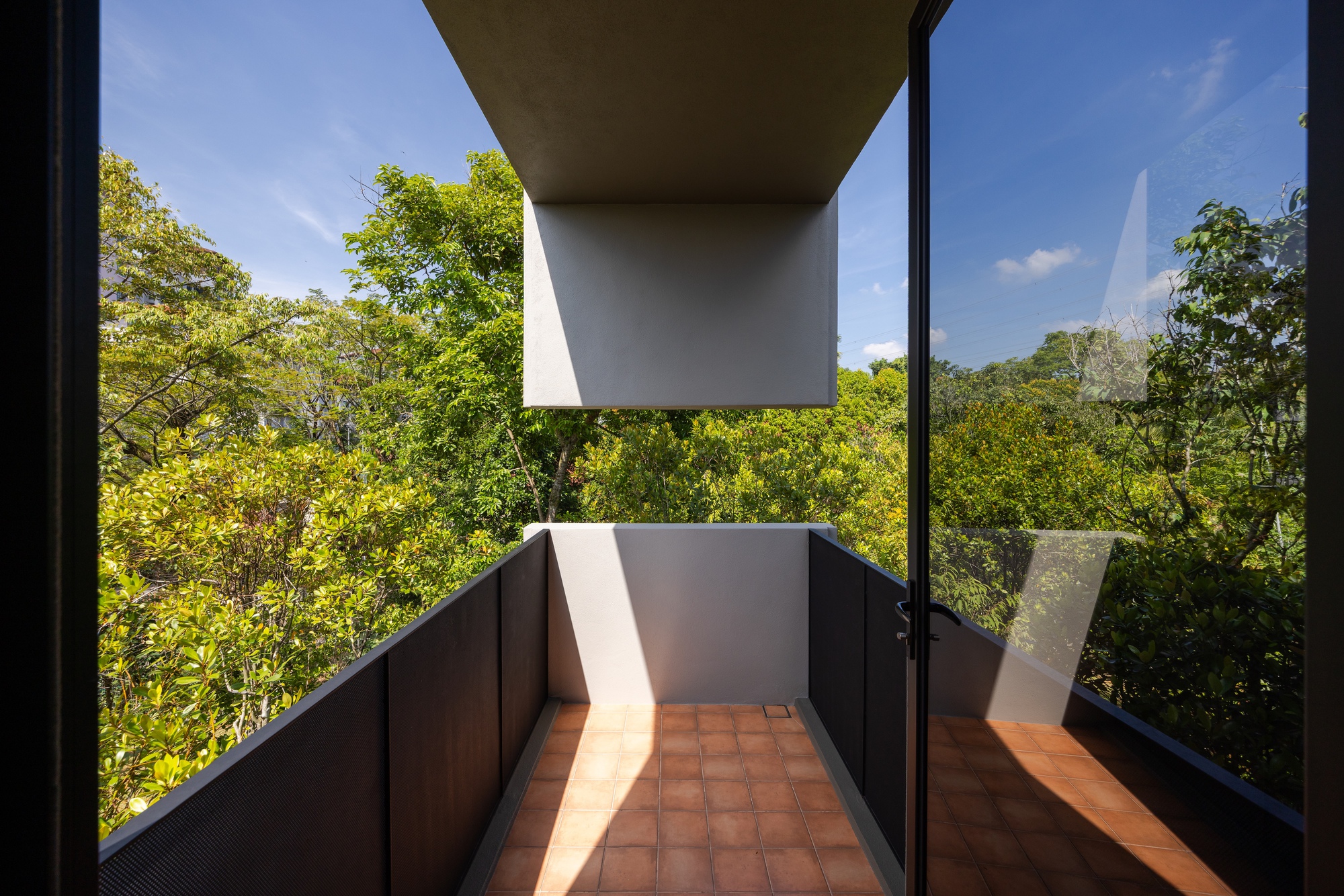 Balcony terrace with terracotta tiles framed by dark metal railings and a view into foliage