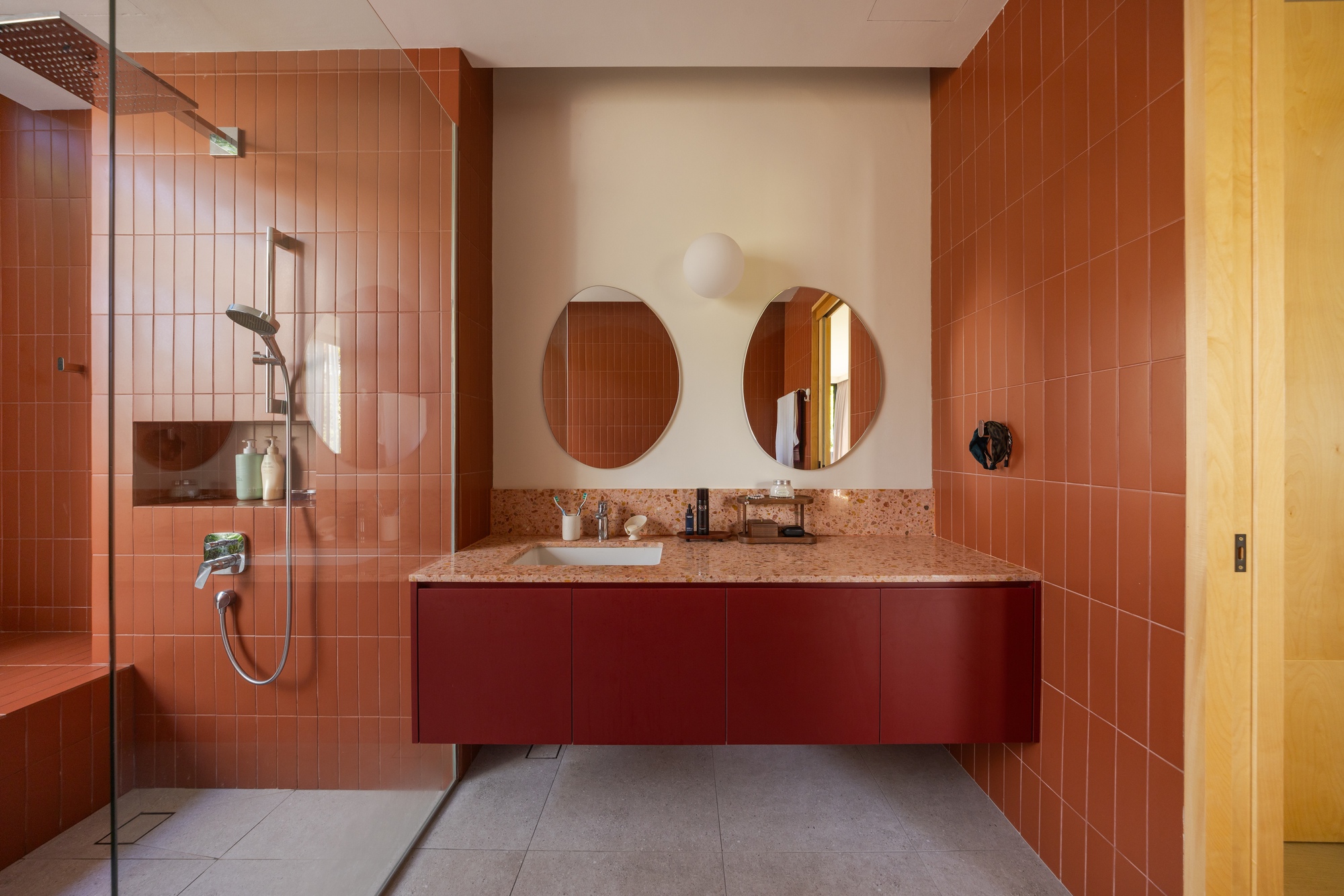 Bathroom with terrazzo vanity, round mirrors, and terracotta tile walls with grey floor tiles