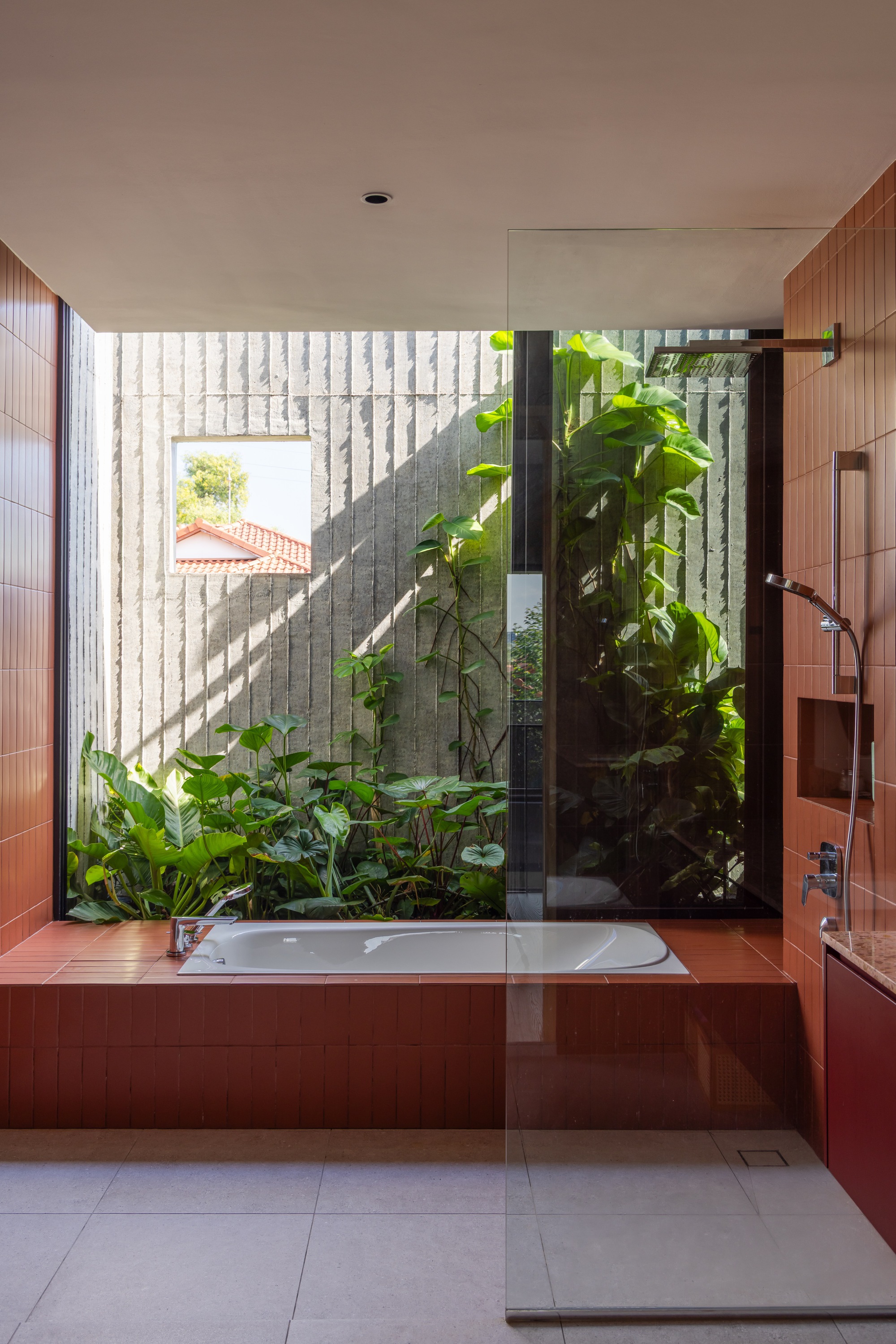 Bathtub with glass screen overlooking a planted courtyard through textured concrete block walls