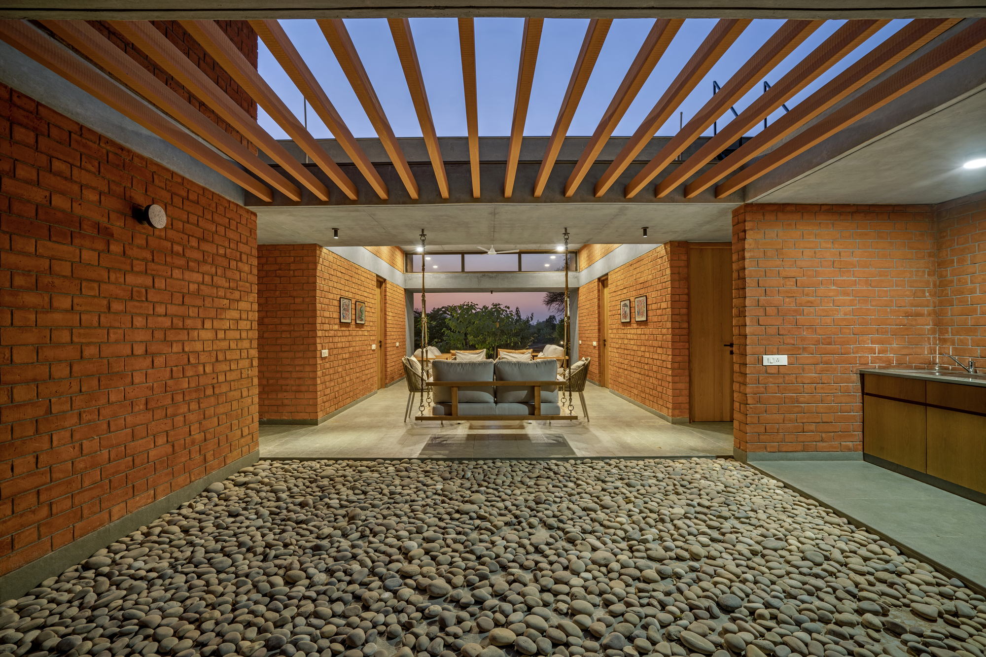 Interior courtyard with timber pergola, exposed rafters and pebbled floor at dusk