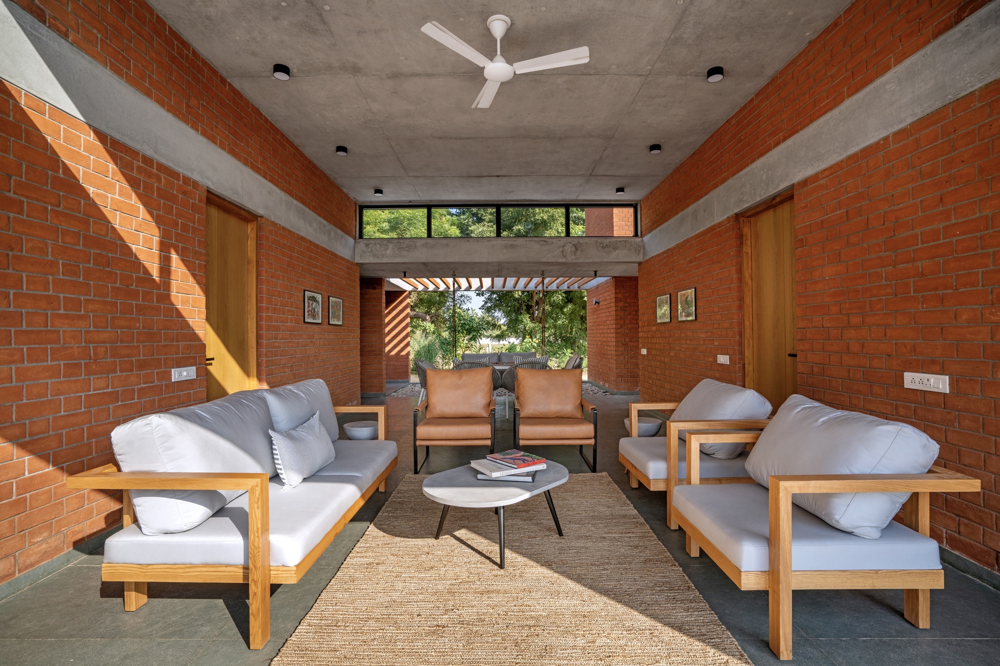 Living room with red brick walls framing a view through a slatted pergola to the landscape beyond