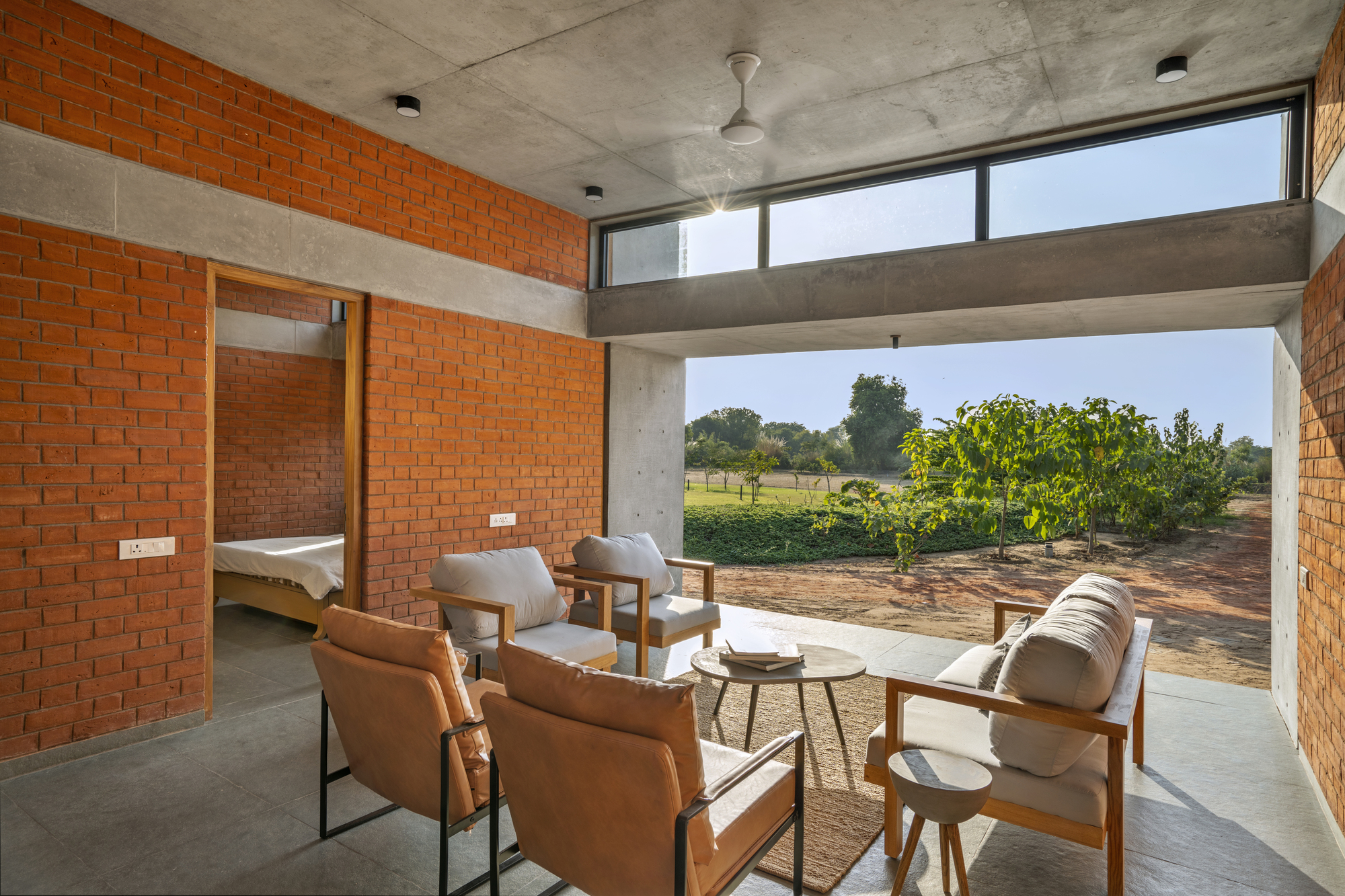 Interior seating area opening to agricultural fields through a wide concrete-framed aperture in morning light