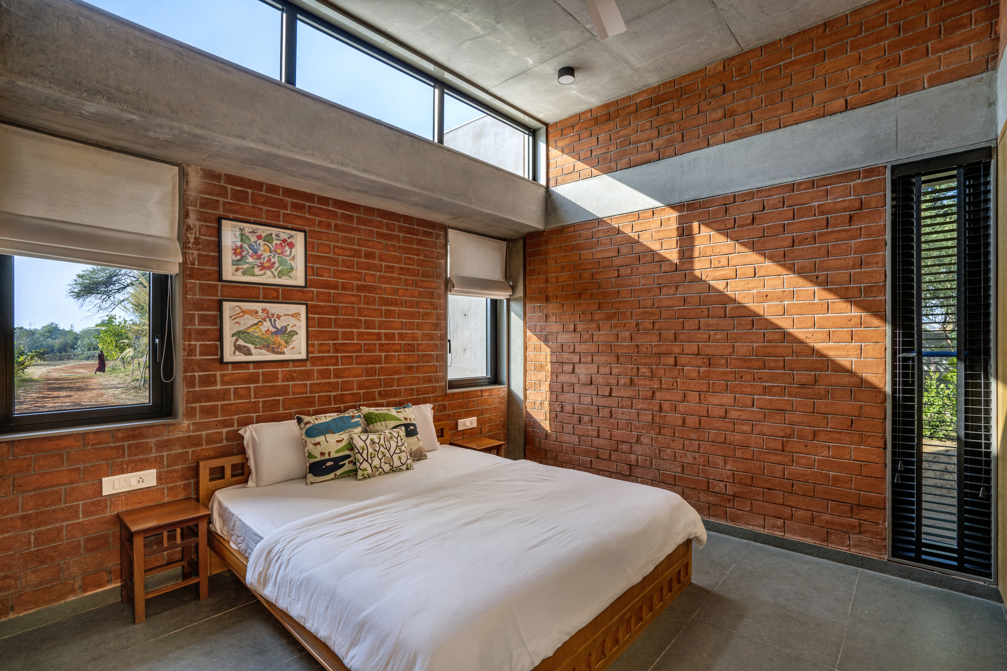 Bedroom with red brick walls, concrete ceiling beam, and clerestory windows casting geometric shadows