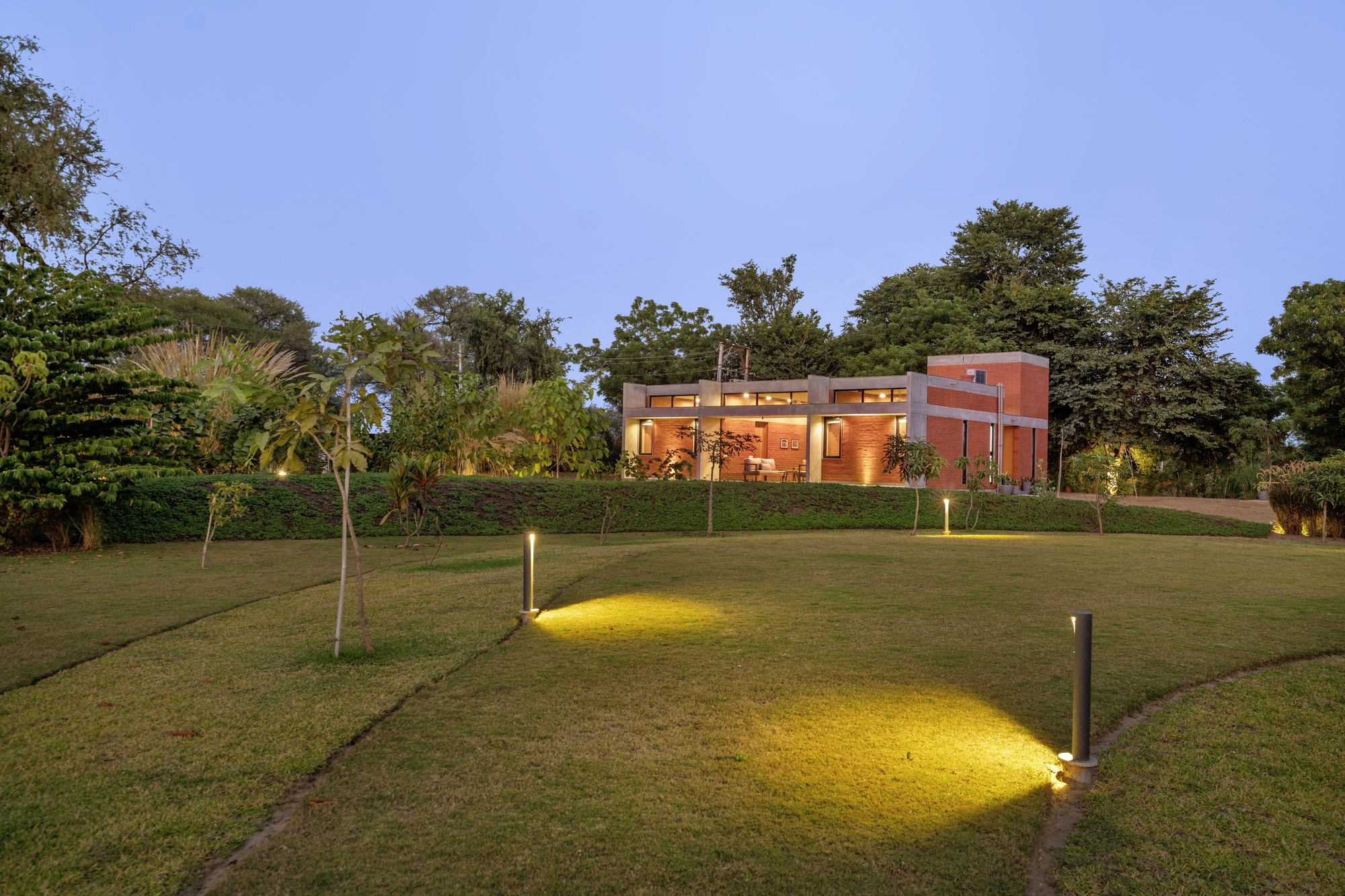 Landscape lighting casting yellow pools across the sloping lawn in early evening