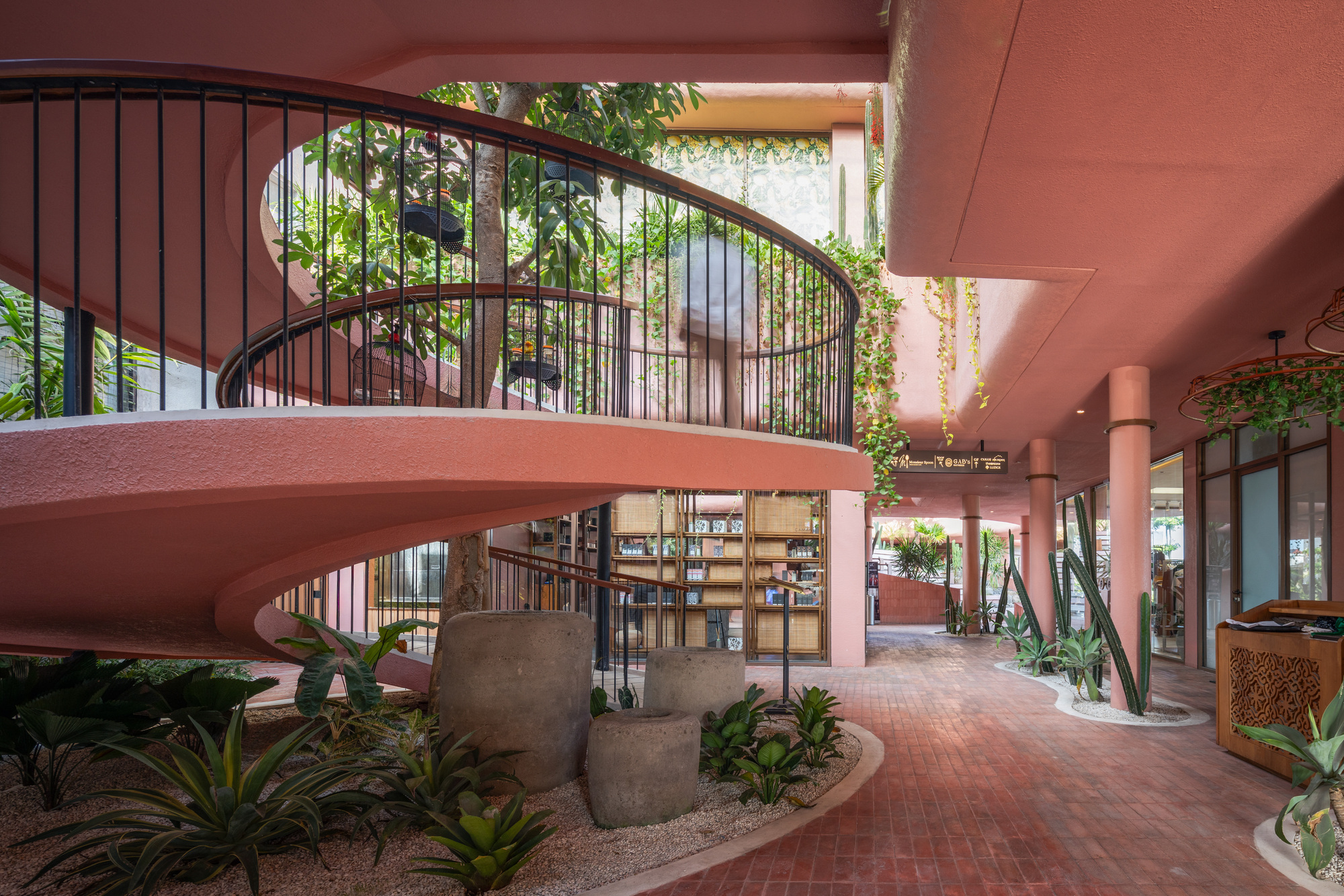Curved staircase with black metal railings rising from the planted interior courtyard below