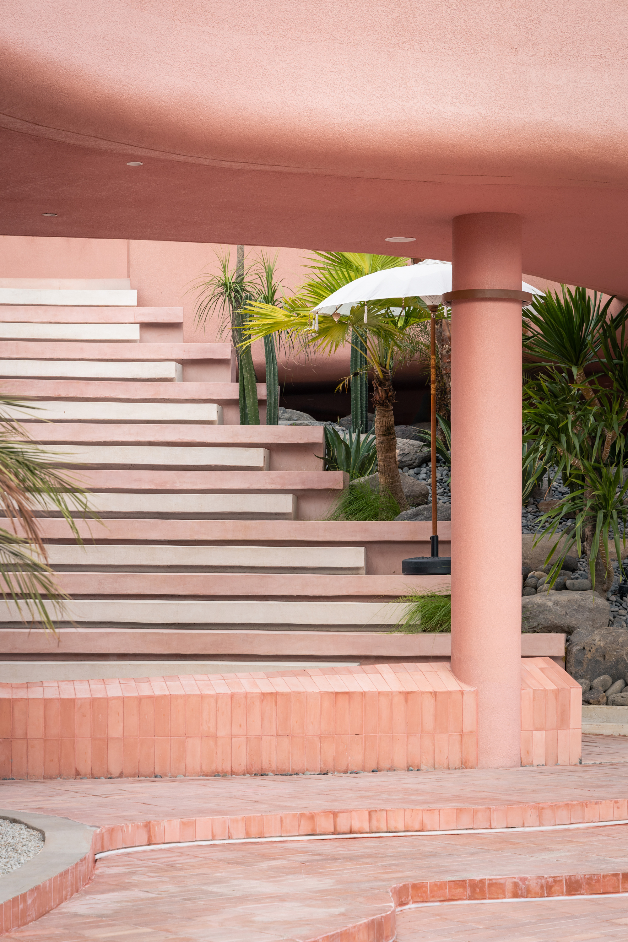 Cantilevered stair treads in pink and white beneath a continuous curved soffit with potted palms and umbrella