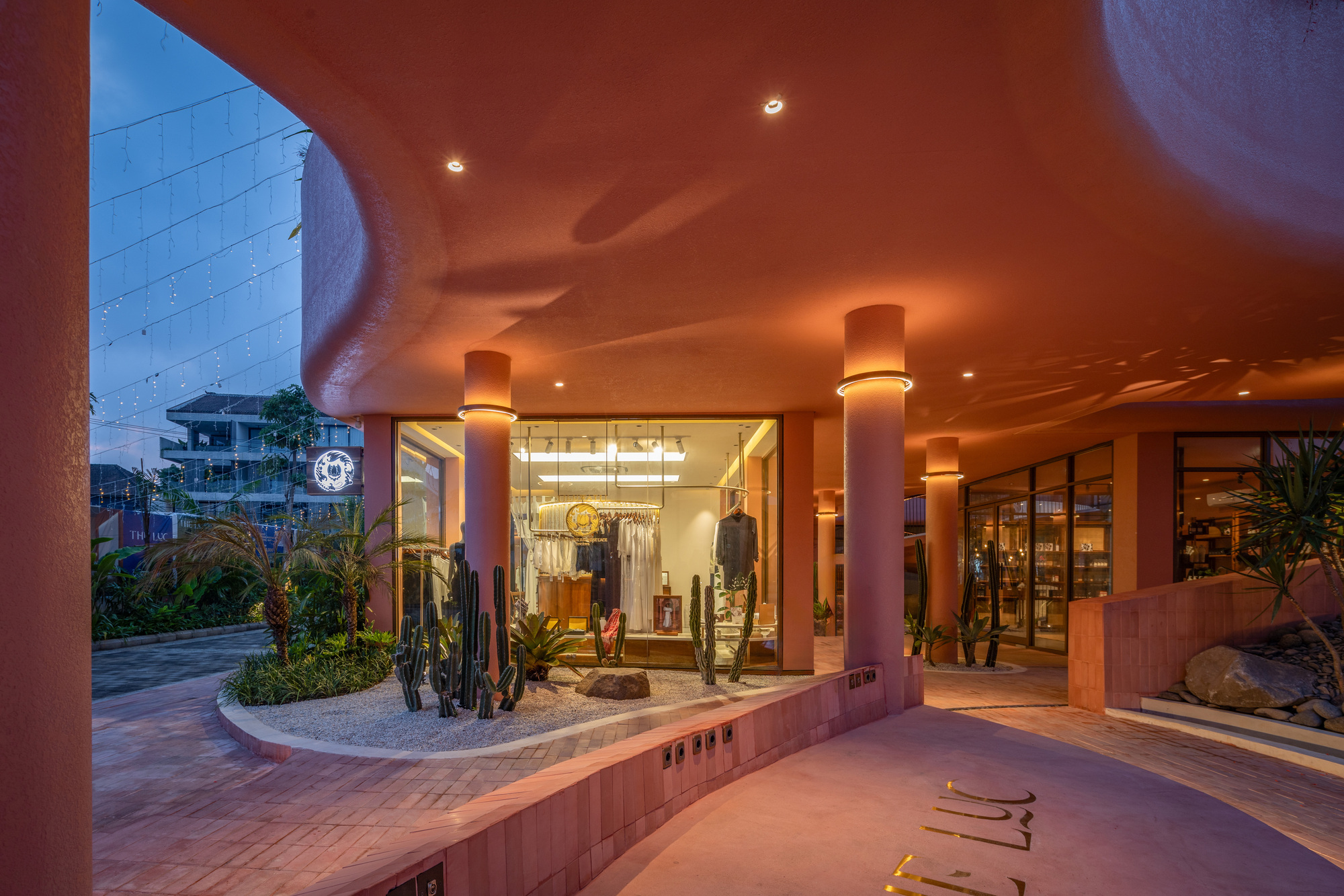 Covered entry colonnade with cylindrical columns and pink ceiling at twilight with retail displays visible beyond