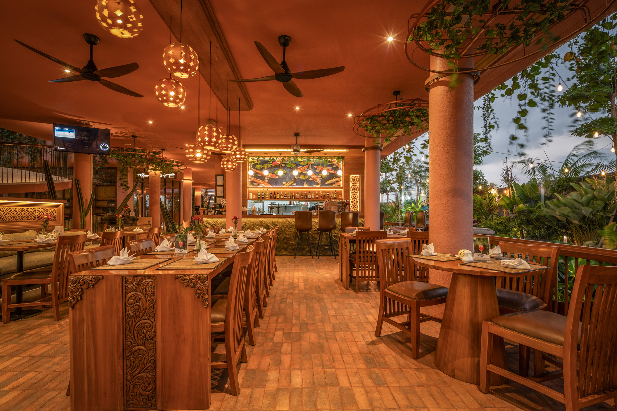 Restaurant interior with carved timber tables and spherical pendant lights under a terracotta ceiling at twilight
