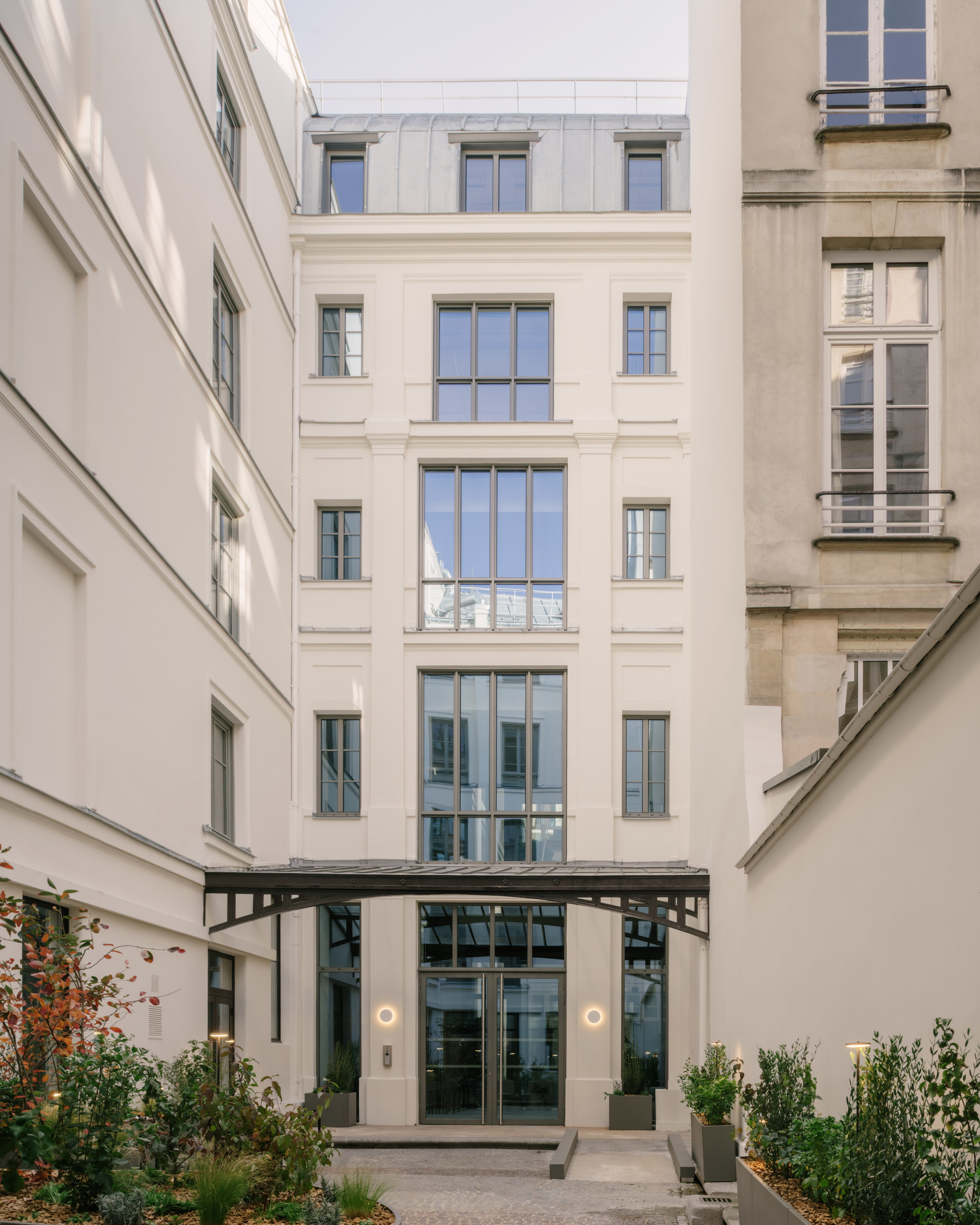 Courtyard entry facade with glazed opening beneath a steel canopy and planted beds on either side