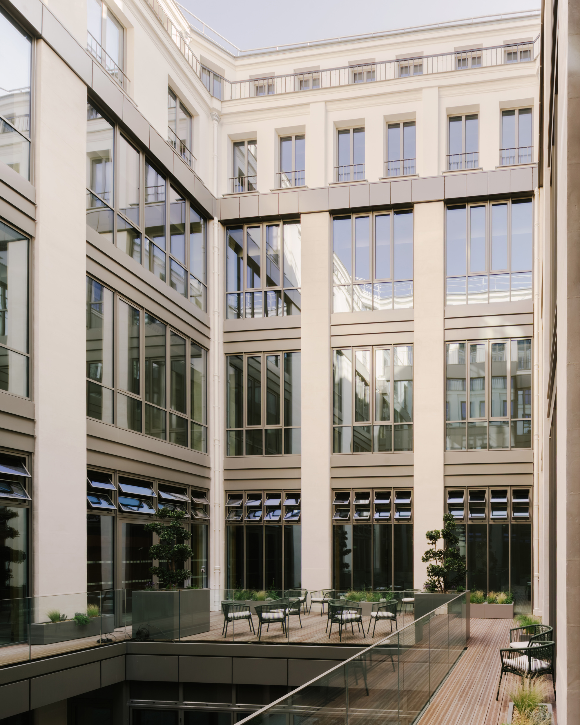 Interior courtyard with glazed facades, horizontal banding, planted beds, and seating on a wooden deck