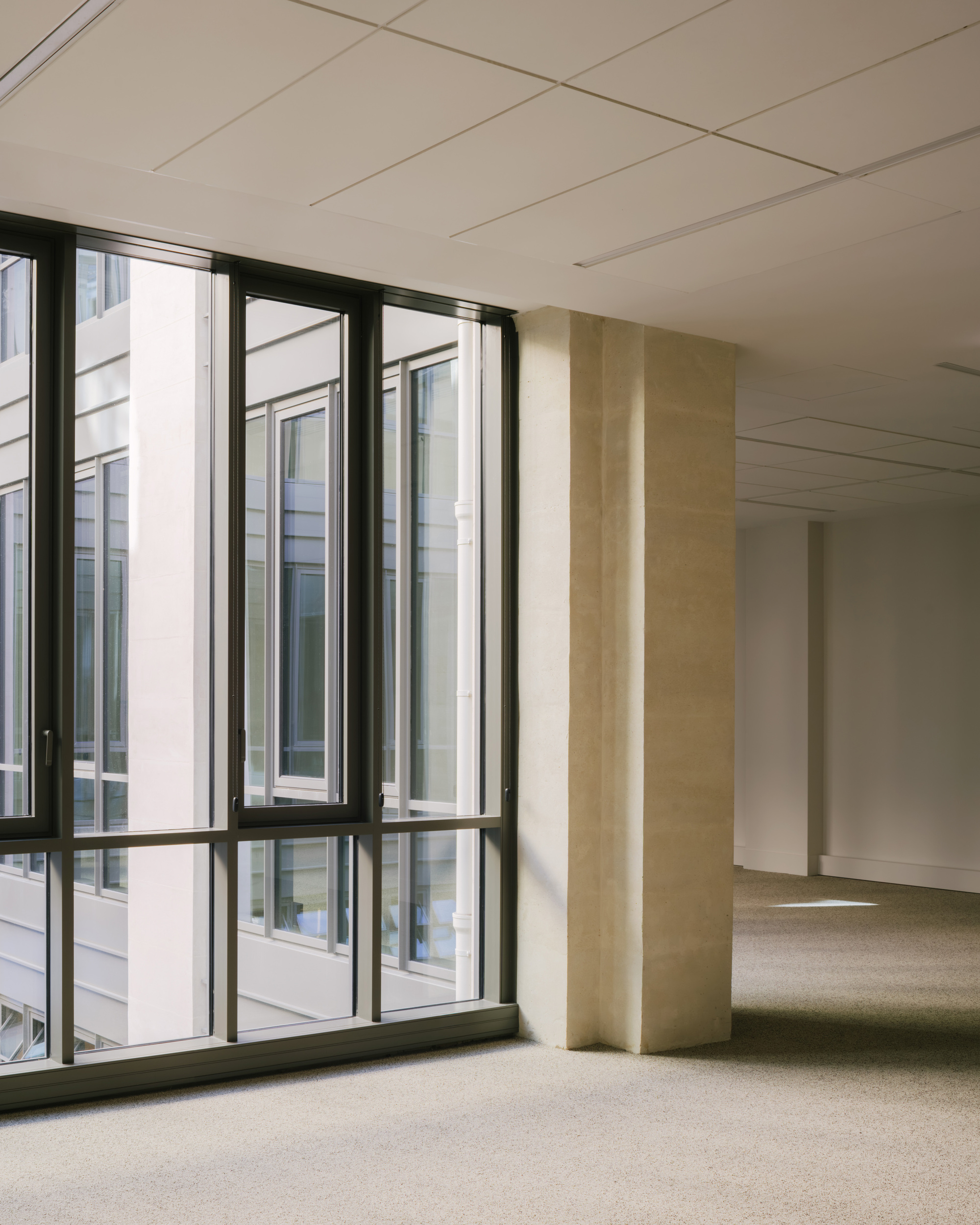 Interior office space with suspended ceiling panels, floor-to-ceiling windows, and vertical concrete columns with striped detailing