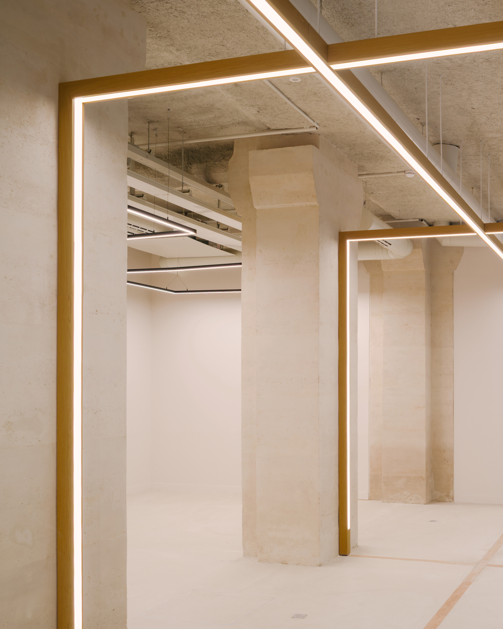 Concrete interior with brass-edged illuminated frames around columns and exposed ceiling services above