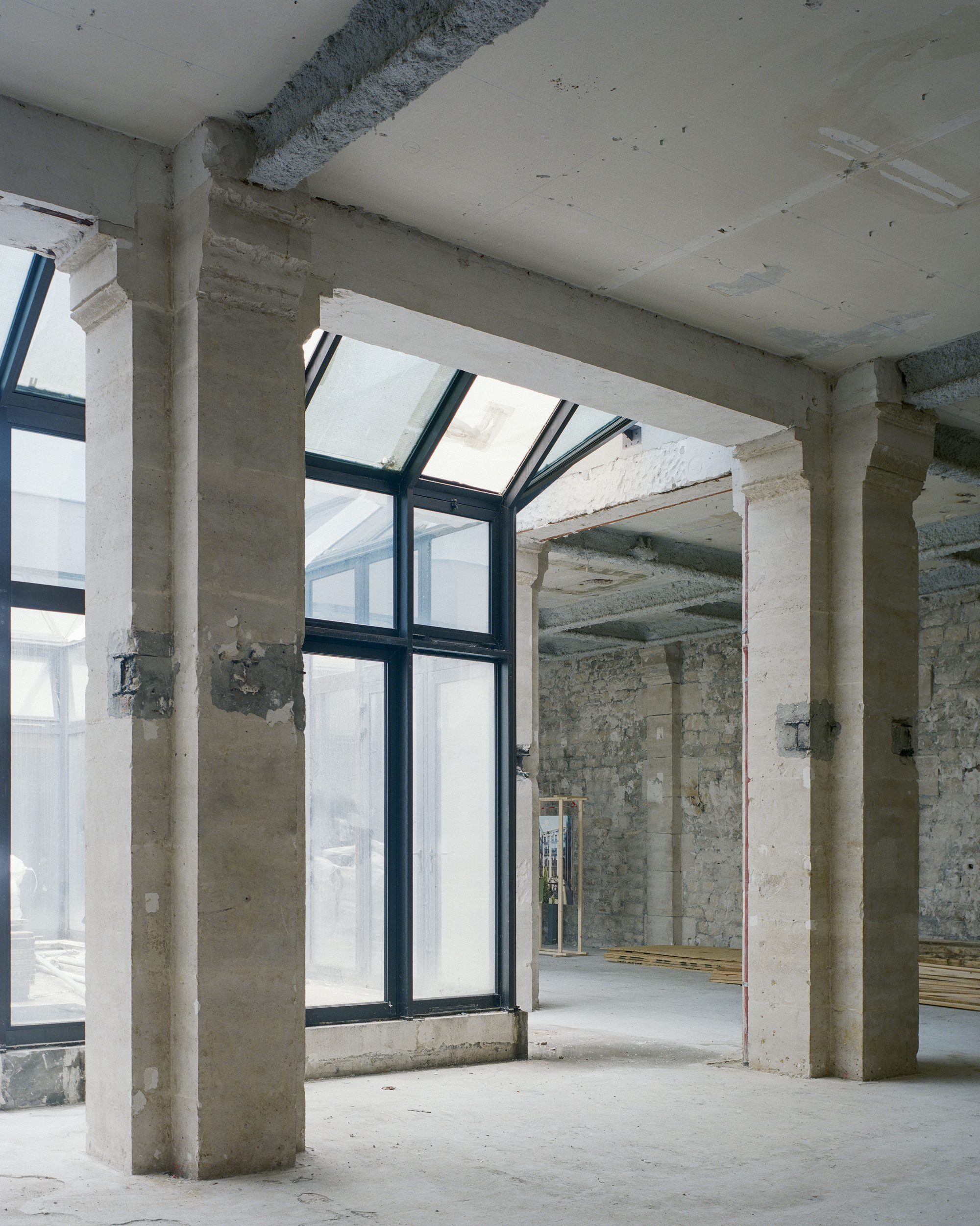 View through concrete columns toward a black-framed glazed opening in the existing structure