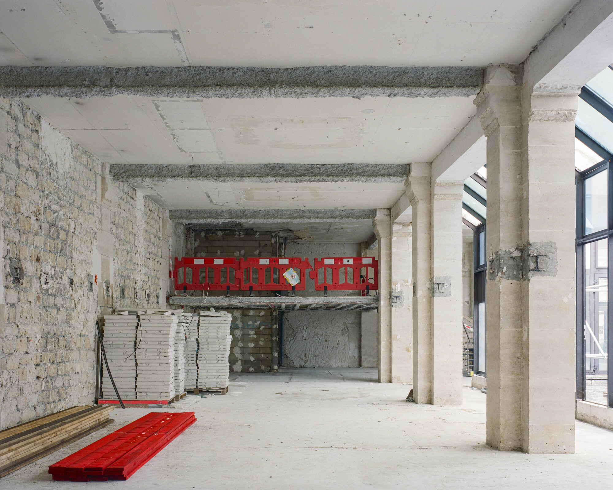 Interior space with exposed brick wall, concrete beams and red safety barriers on mezzanine