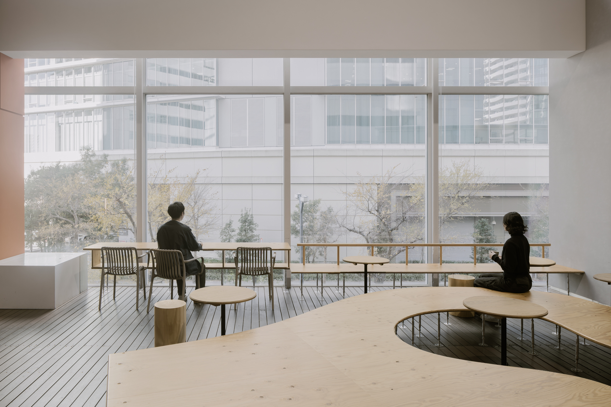 Timber deck terrace with curved table and two seated figures overlooking snow-covered trees