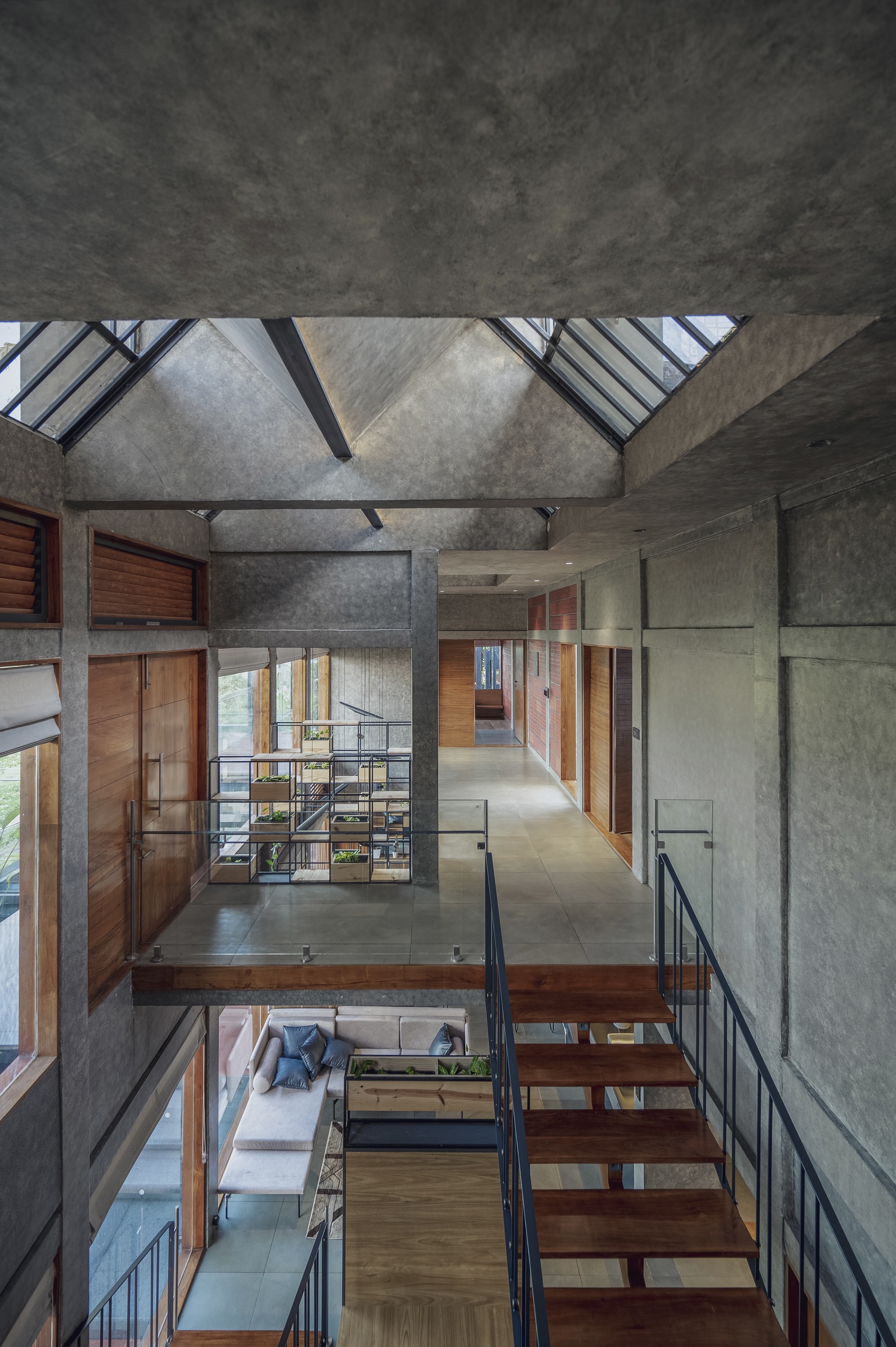 Double-height interior with exposed concrete walls and timber walkways beneath a clerestory skylight