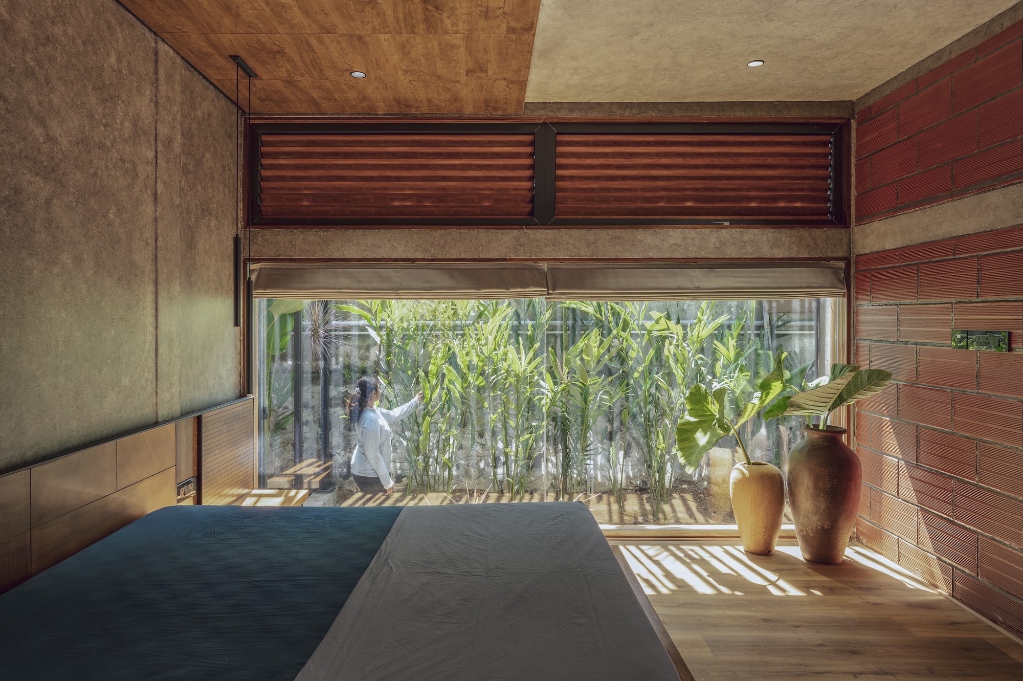 Bedroom corner with floor-to-ceiling glazing opening to a bamboo courtyard in dappled sunlight