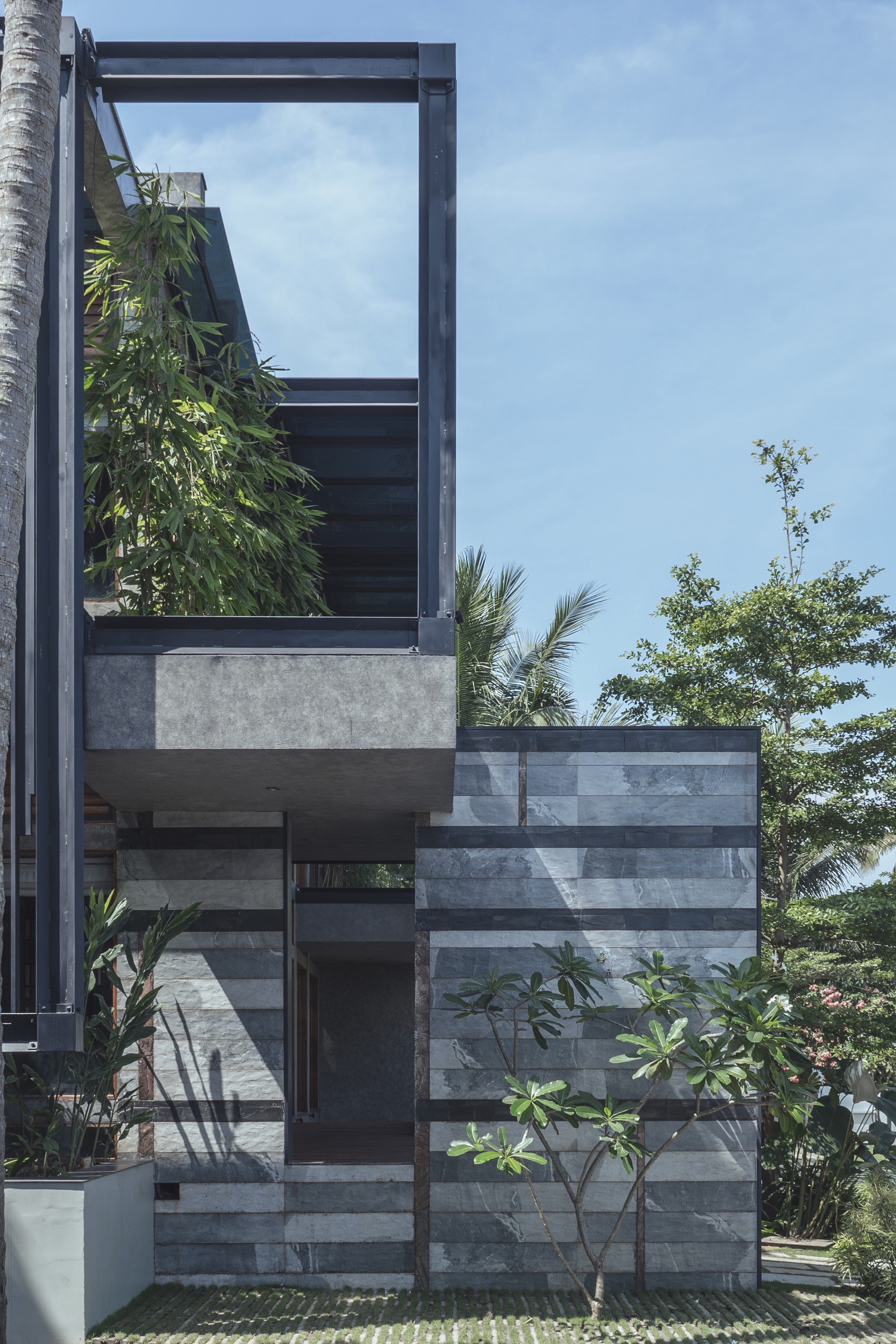 Exterior view of striped stone facade with cantilevered steel frame and vertical greenery beneath a clear sky