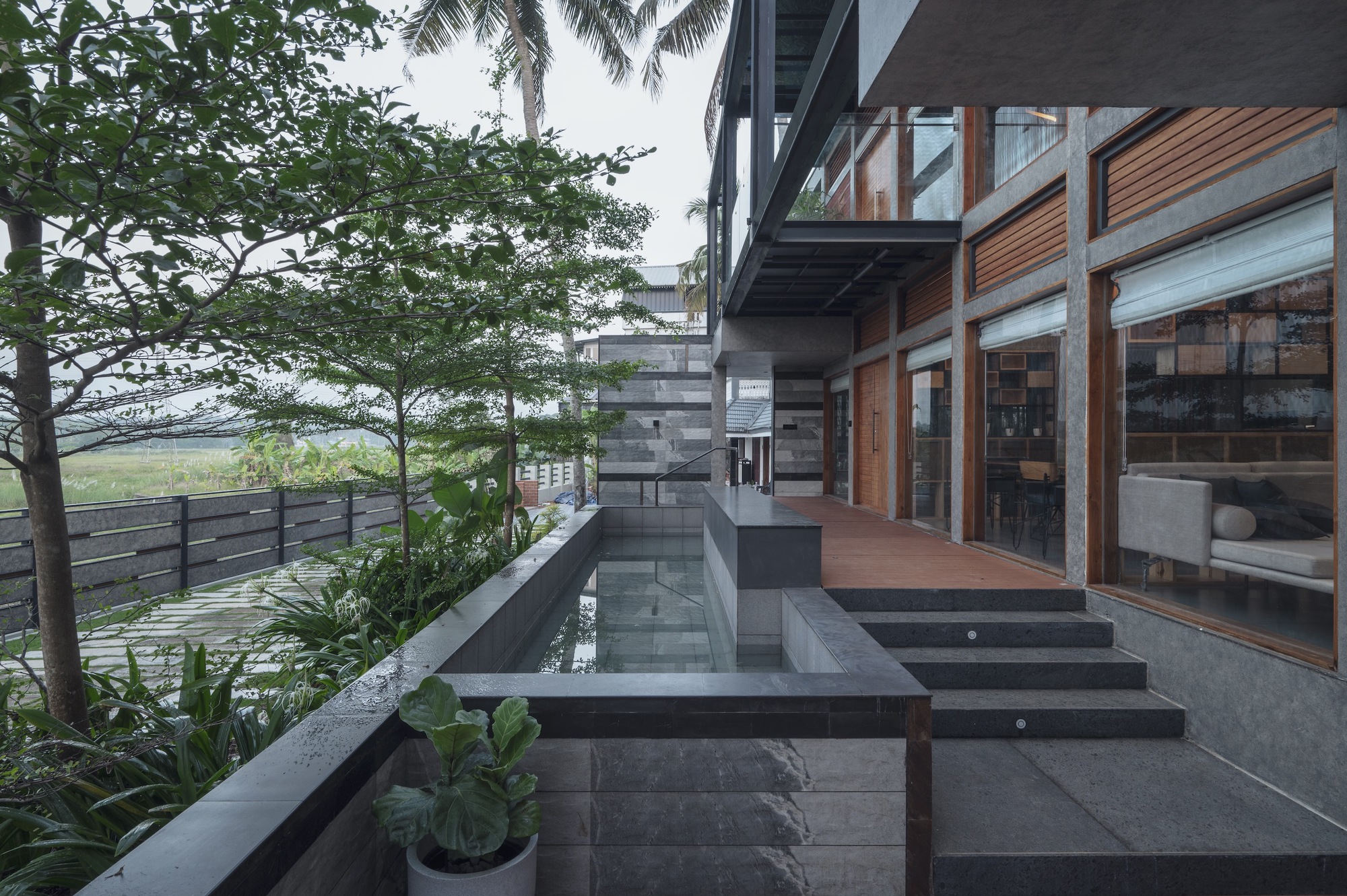 Stepped terrace with dark stone slabs and shallow water channel alongside timber and glass facade