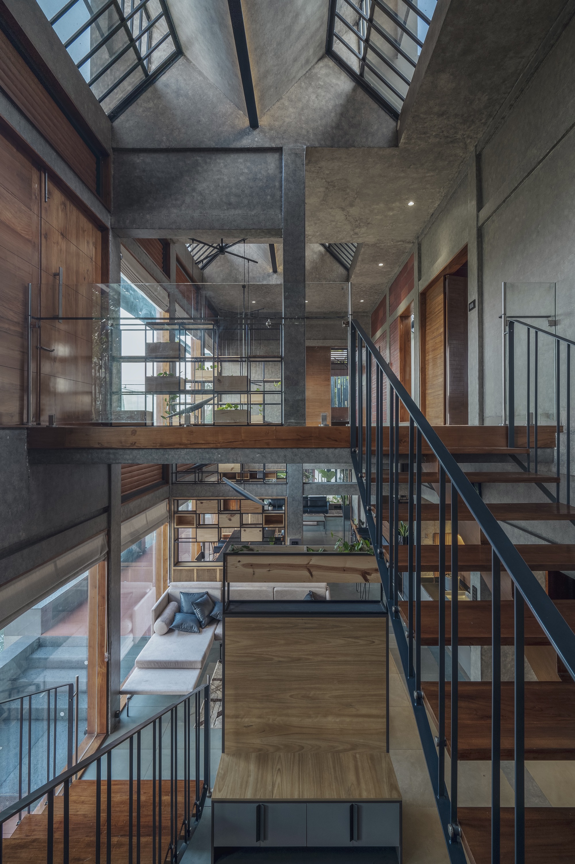 Double-height interior void with timber and steel stairs connecting stacked platforms under concrete ceiling