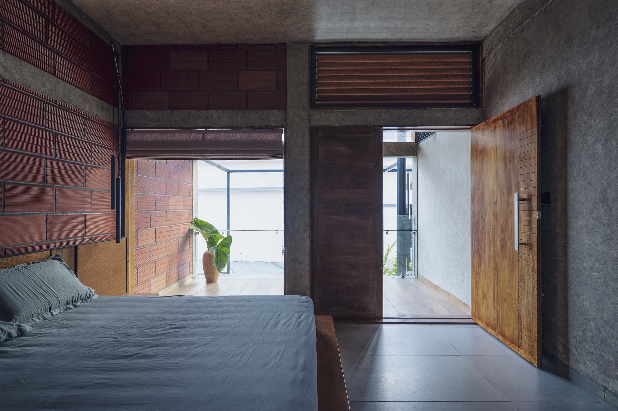 Bedroom with exposed brick wall and polished concrete floor opening to corridor beyond timber door