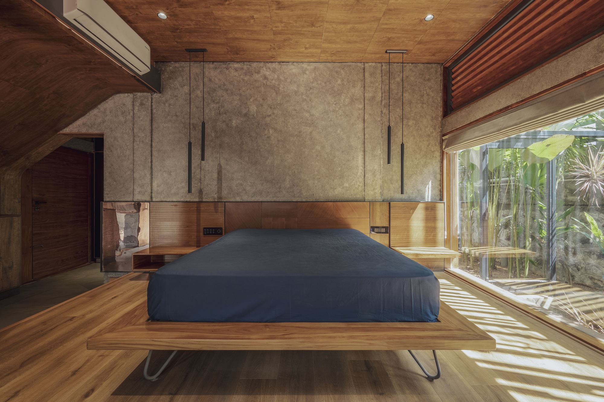Bedroom with platform bed and timber ceiling receiving dappled sunlight through glazed wall to planted courtyard