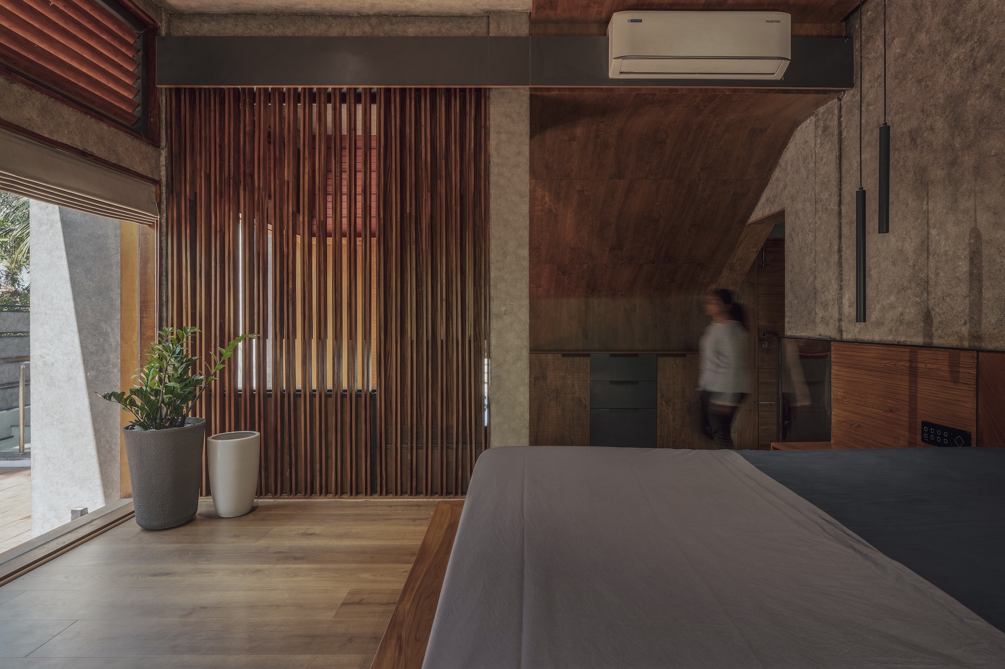 Interior view of vertical timber slat partition beside concrete walls with a blurred figure passing through