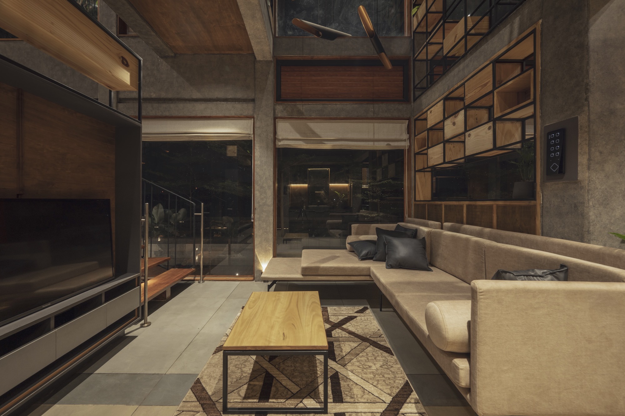 Double-height living room with exposed concrete beams and geometric timber storage wall at dusk