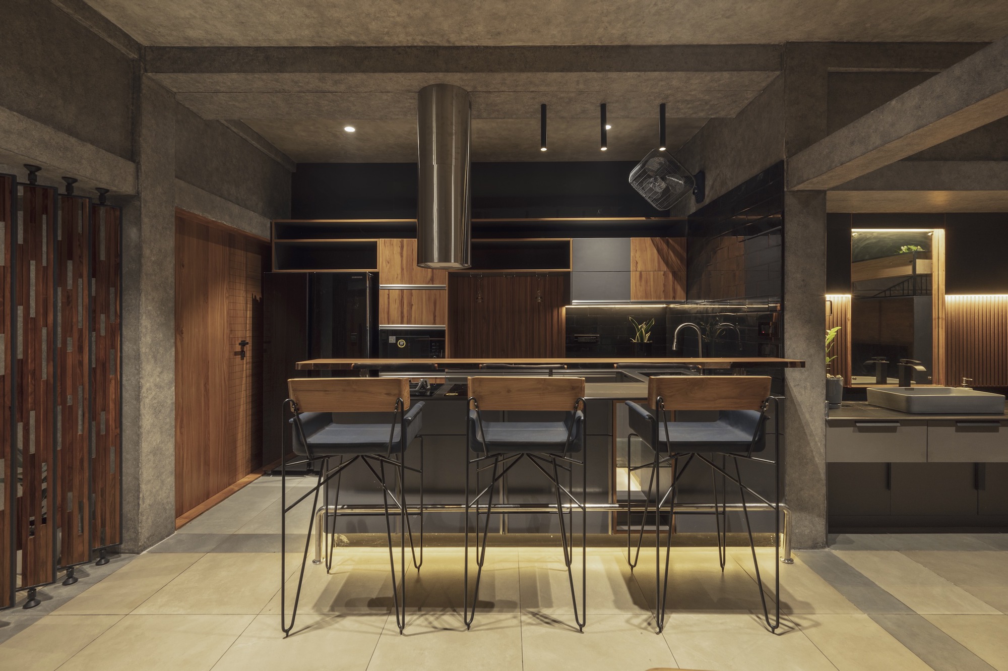 Open kitchen with central island and wire-frame stools under recessed concrete ceiling at night