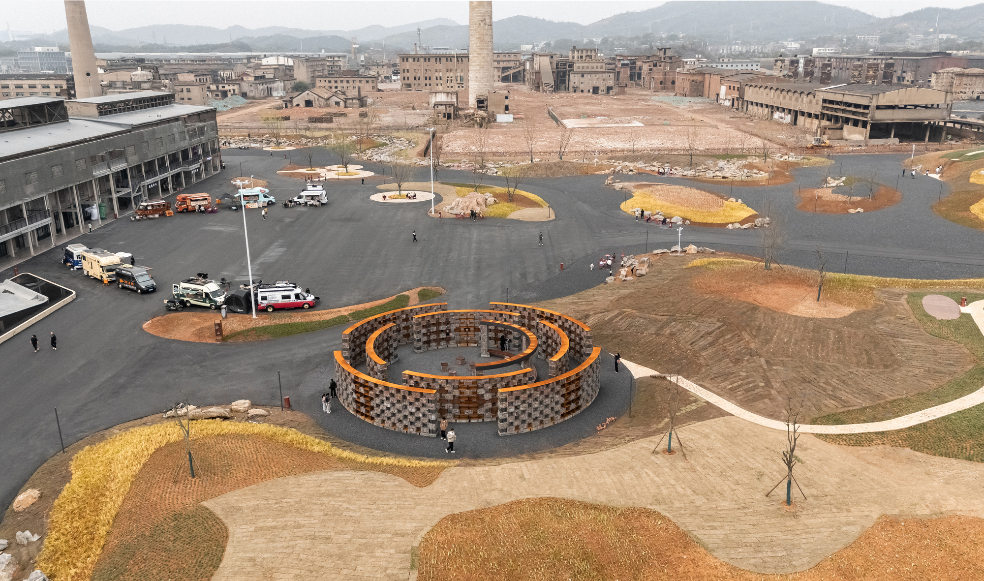 Aerial view of the circular pavilion set within a parking area beside derelict industrial buildings