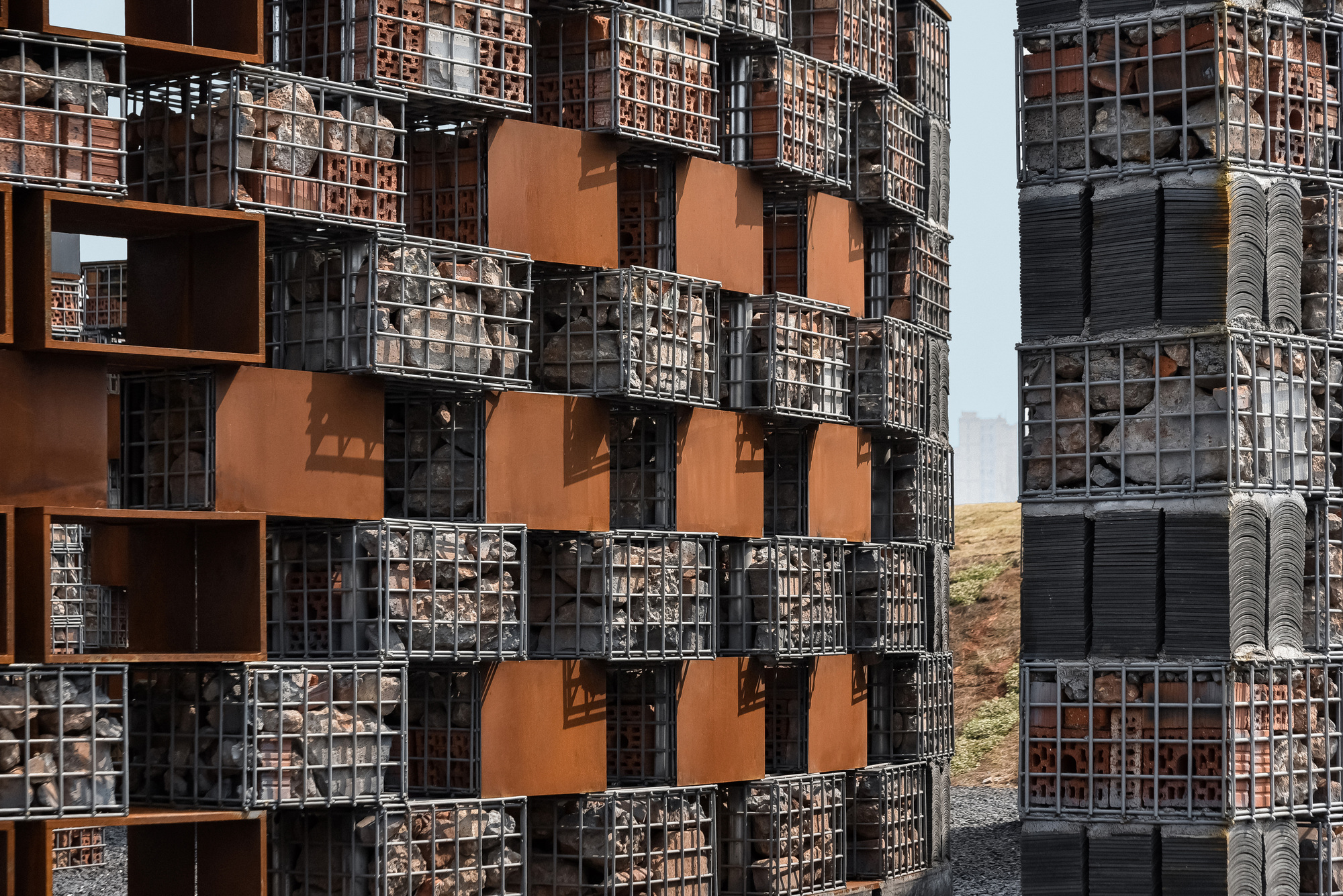 Chequered facade of gabion modules and corten panels casting shadows in bright sunlight