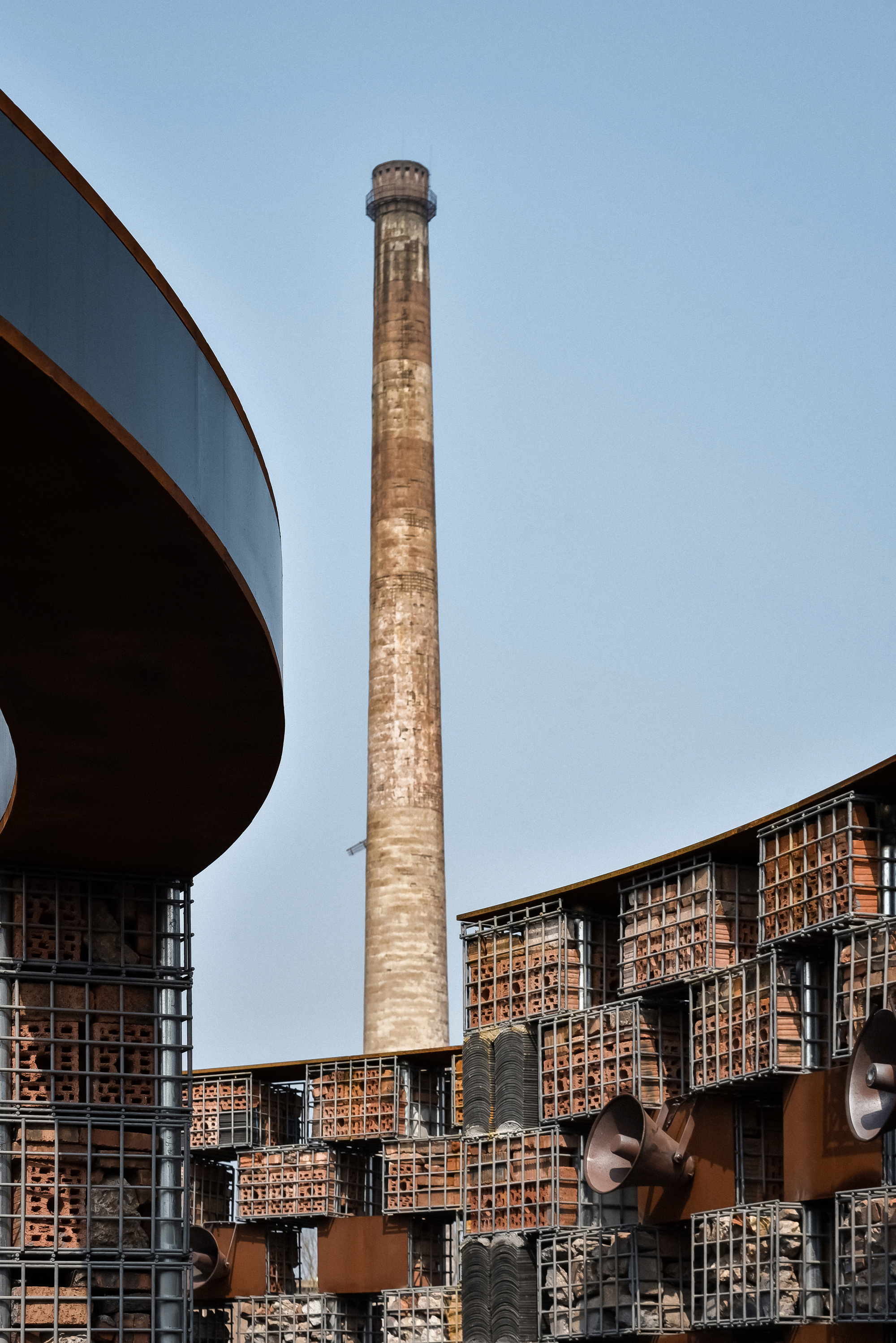 Weathered brick chimney rising behind a curving canopy and gridded brick screen wall with corten steel frames