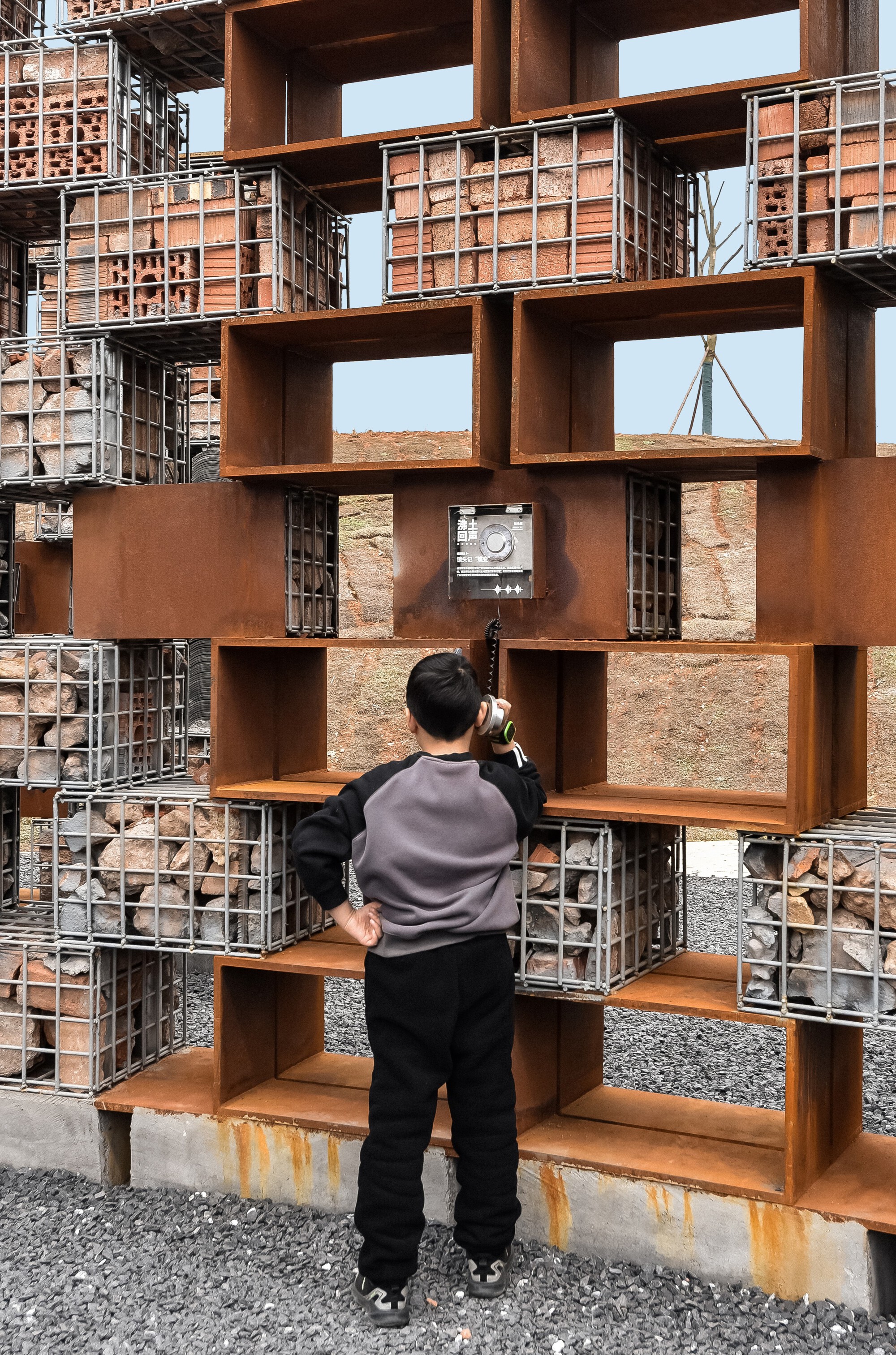Visitor photographing through layered weathered steel box frames and brick infill panels