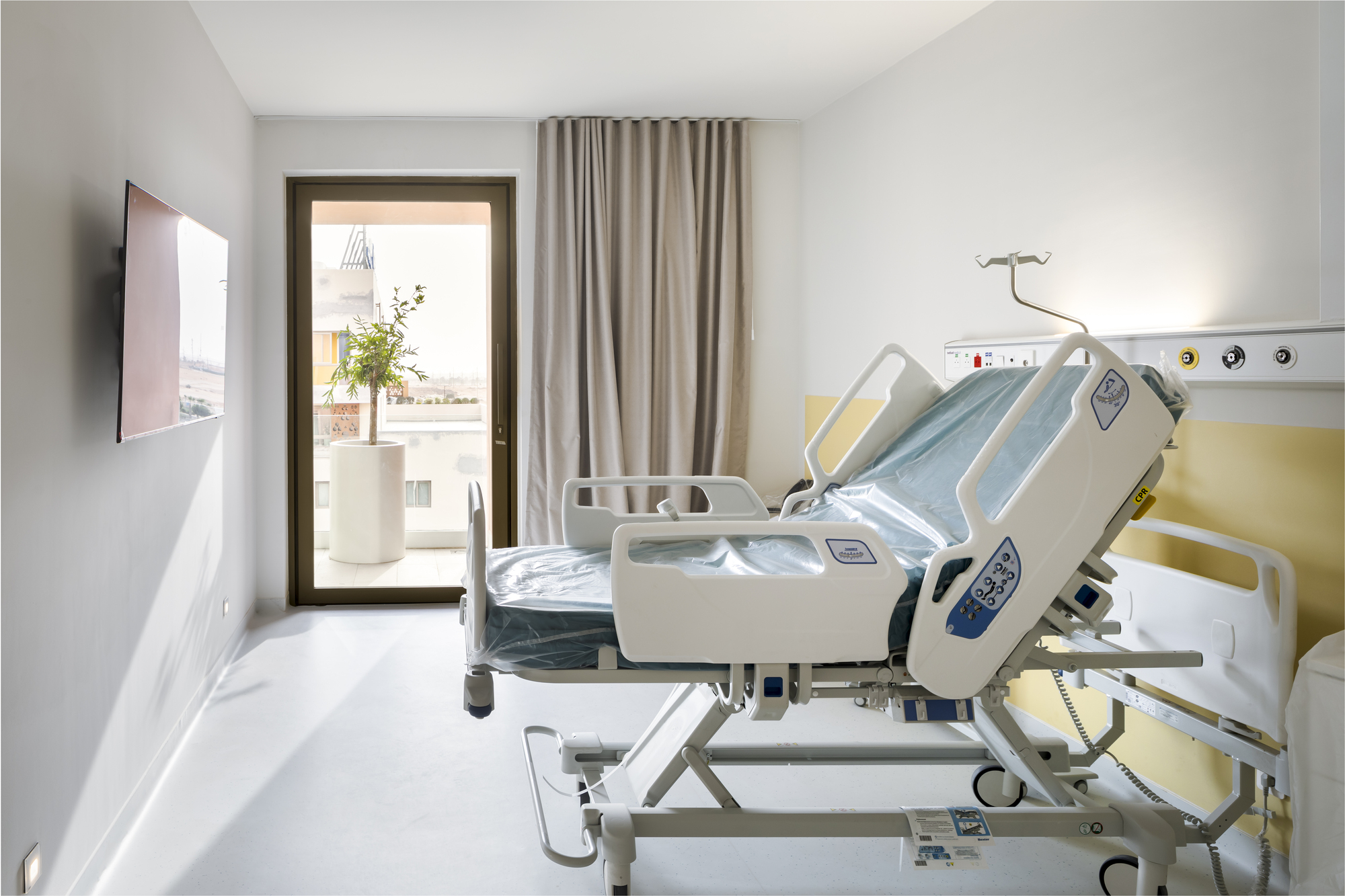 Patient room with adjustable bed, yellow headwall panel and glazed door to terrace