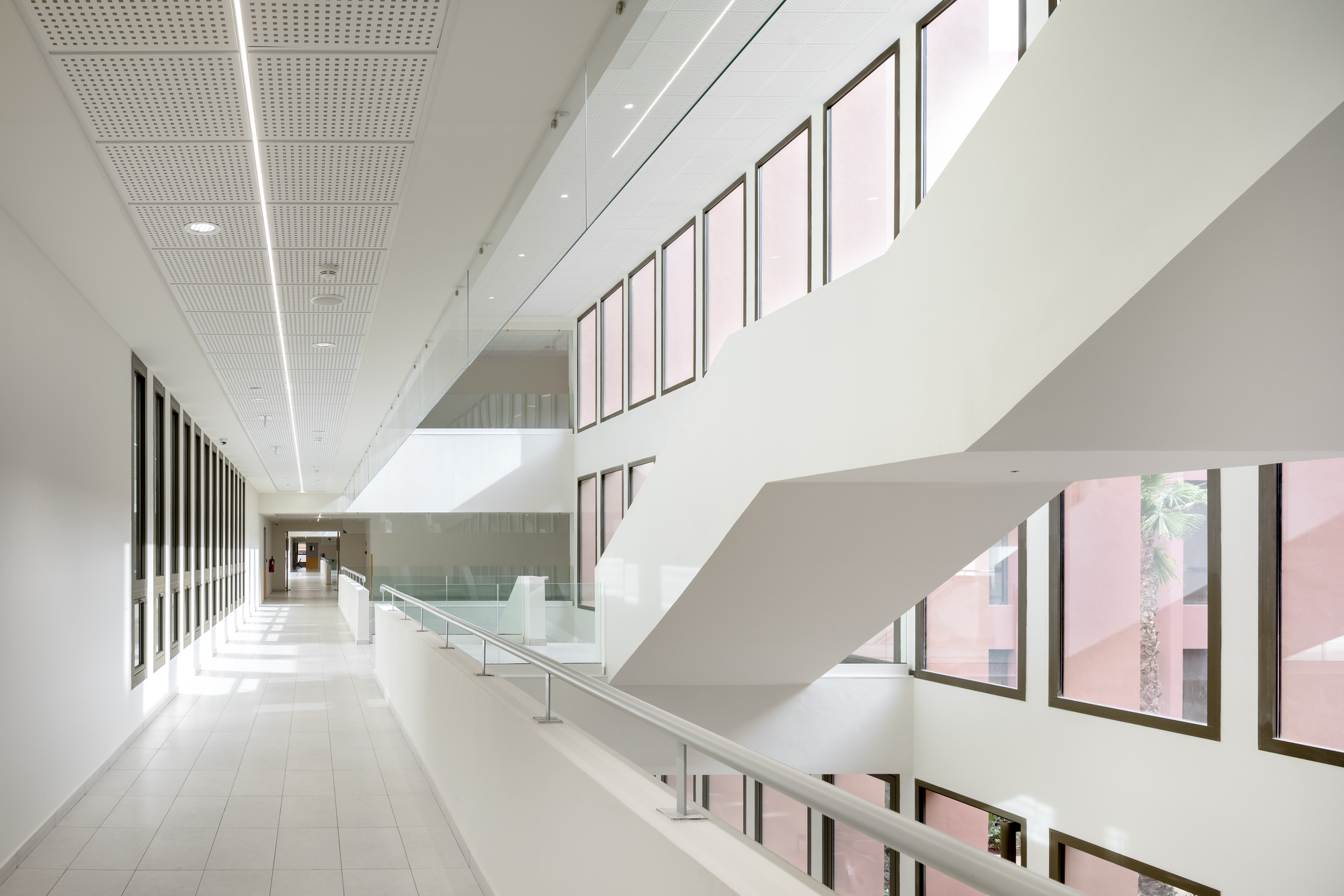 Multilevel circulation space with glass balustrades and pink courtyard views through vertical windows