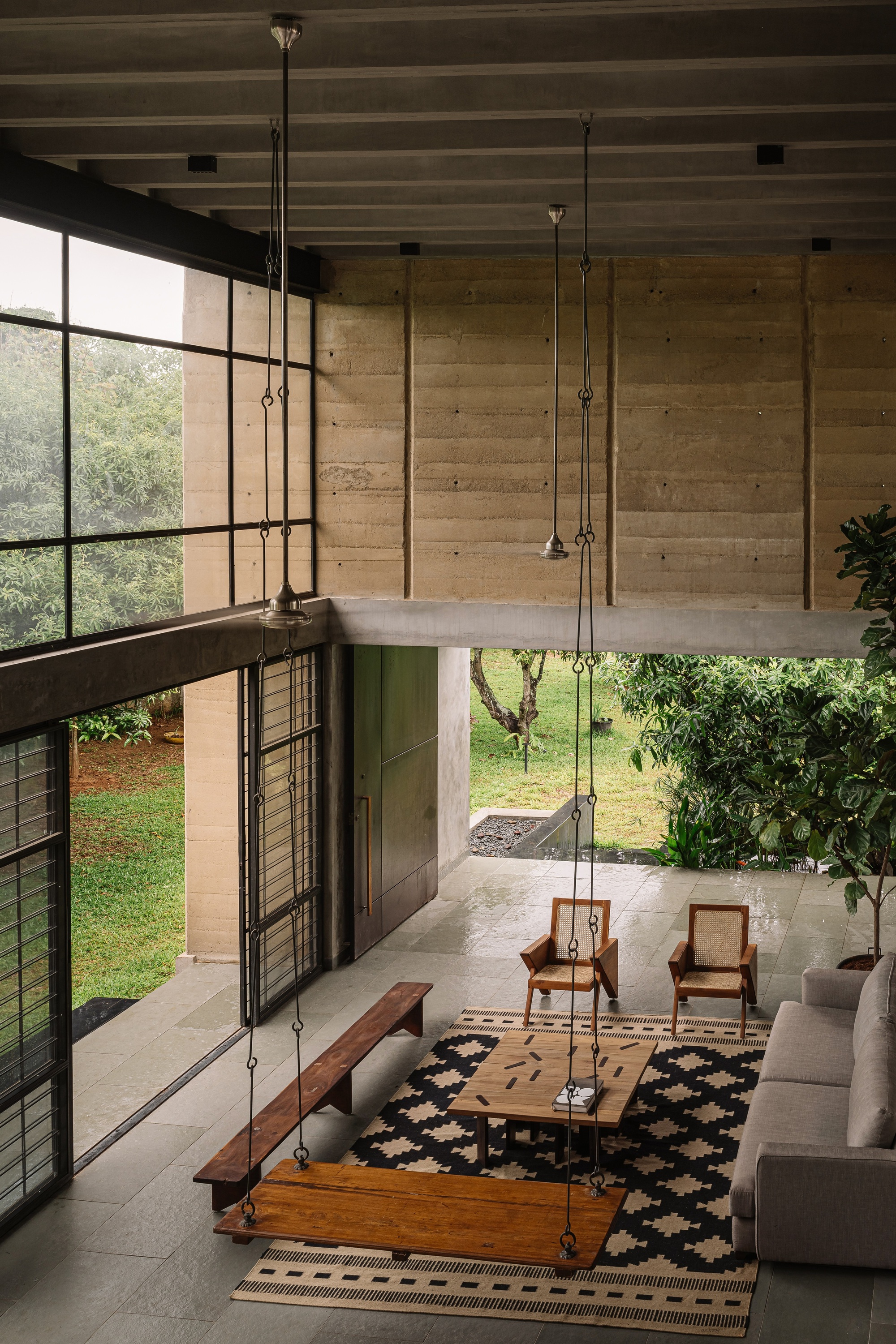 Double-height living room with exposed concrete ceiling joists and suspended swing seat overlooking the garden