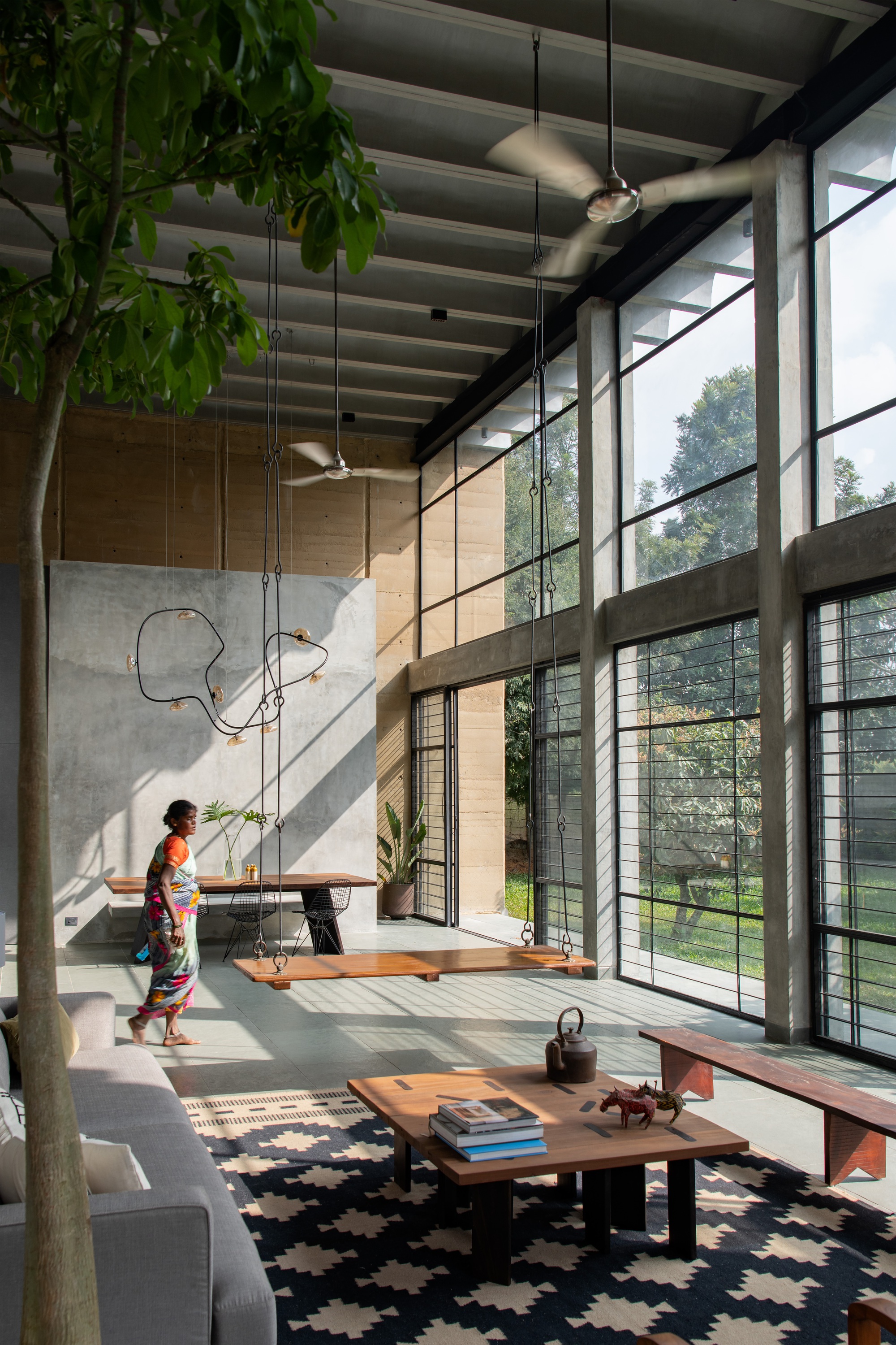 Interior view with person walking past the dining area as sunlight filters through steel-framed windows