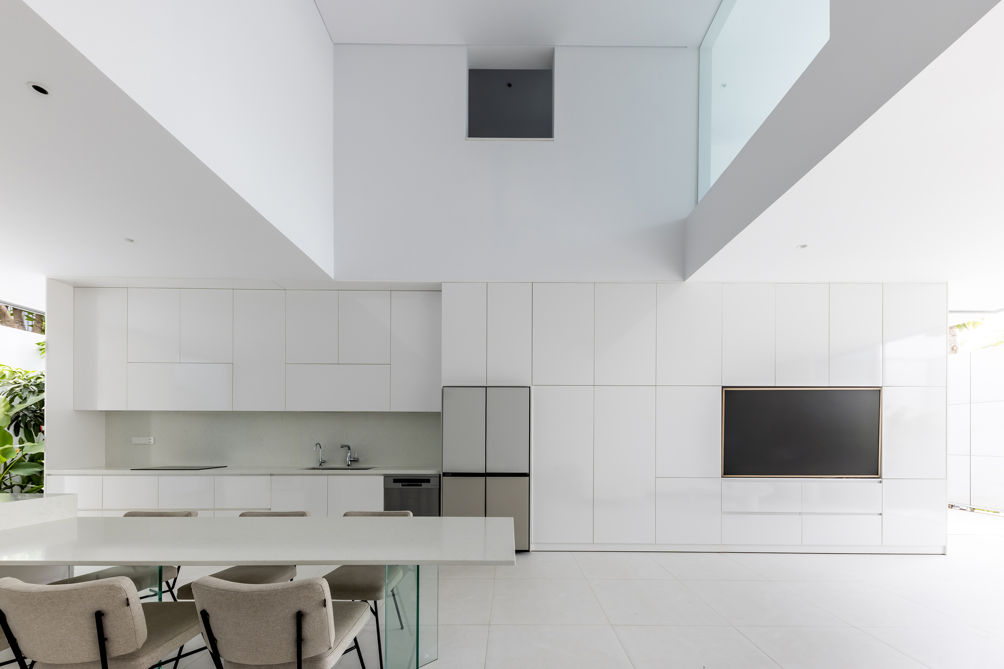 Double height void above the white kitchen and dining table with view to upper skylight