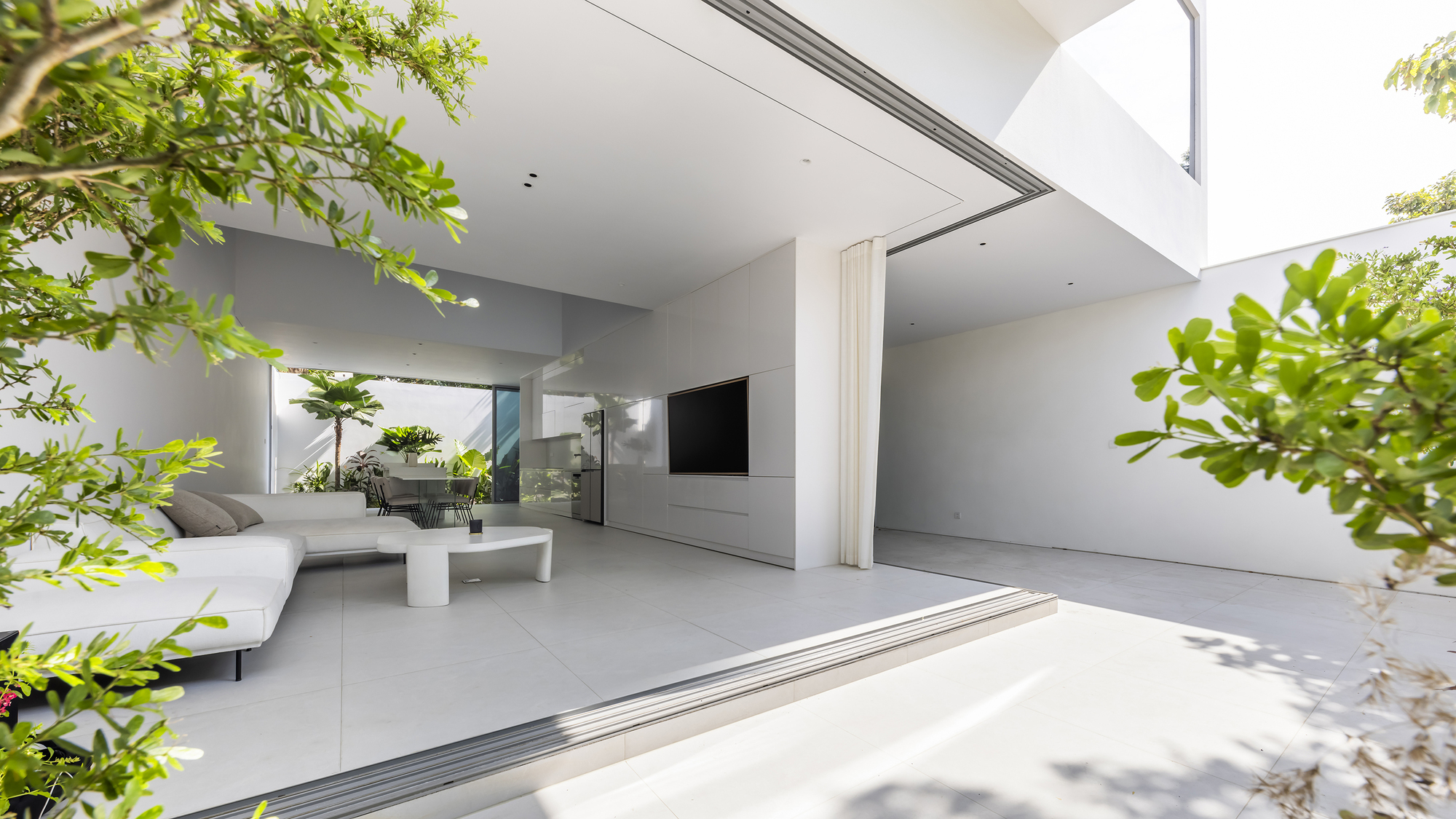 Open living space with sliding glass doors framed by tropical planting in dappled sunlight