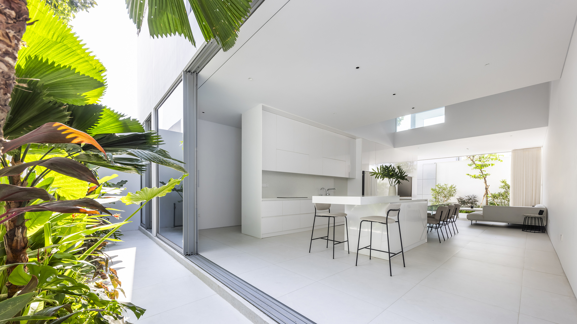 Kitchen island with bar stools opening to dining area and courtyard garden with palm fronds