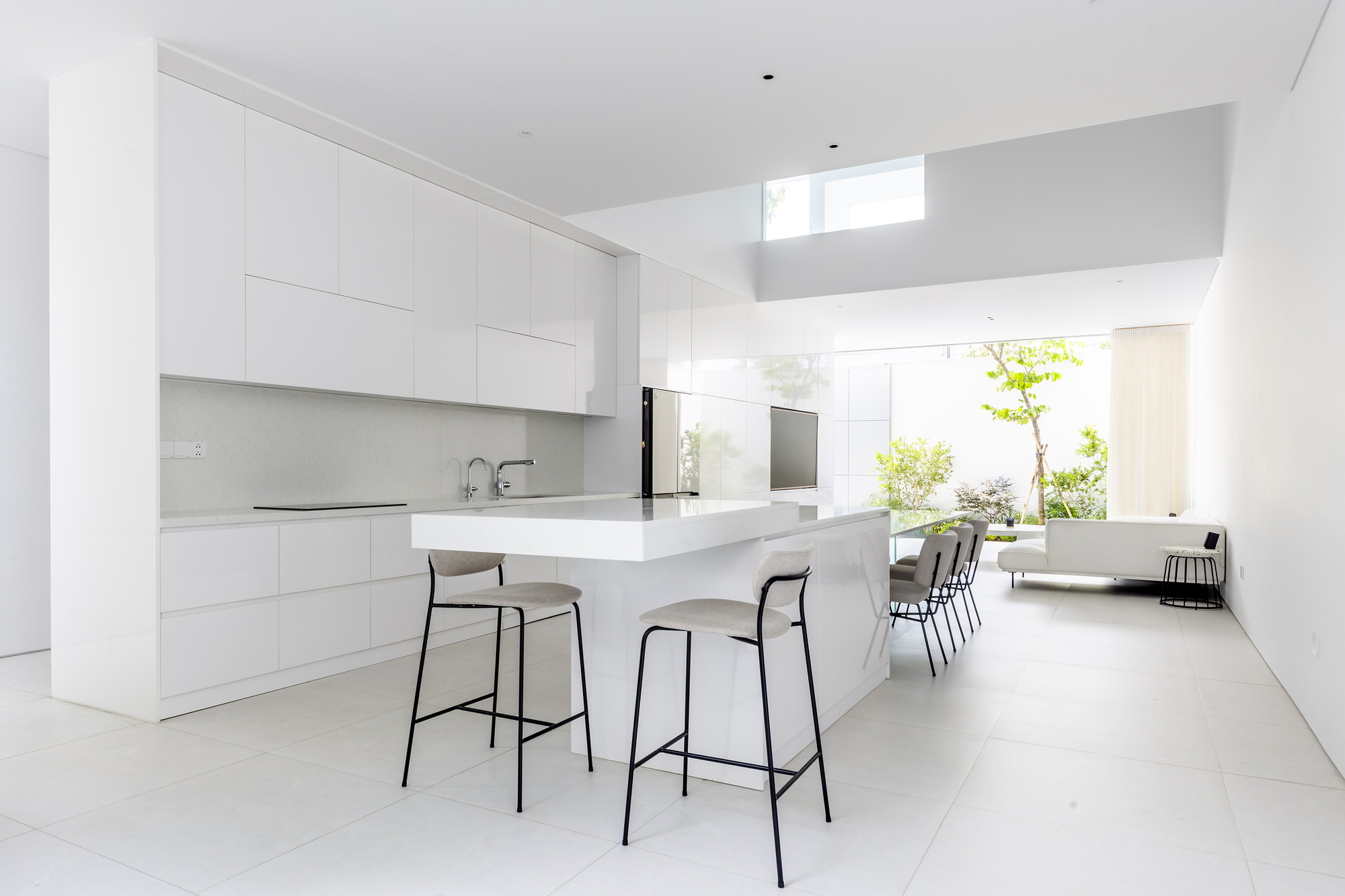 Kitchen with white cabinetry and island beneath clerestory window with view to planted courtyard