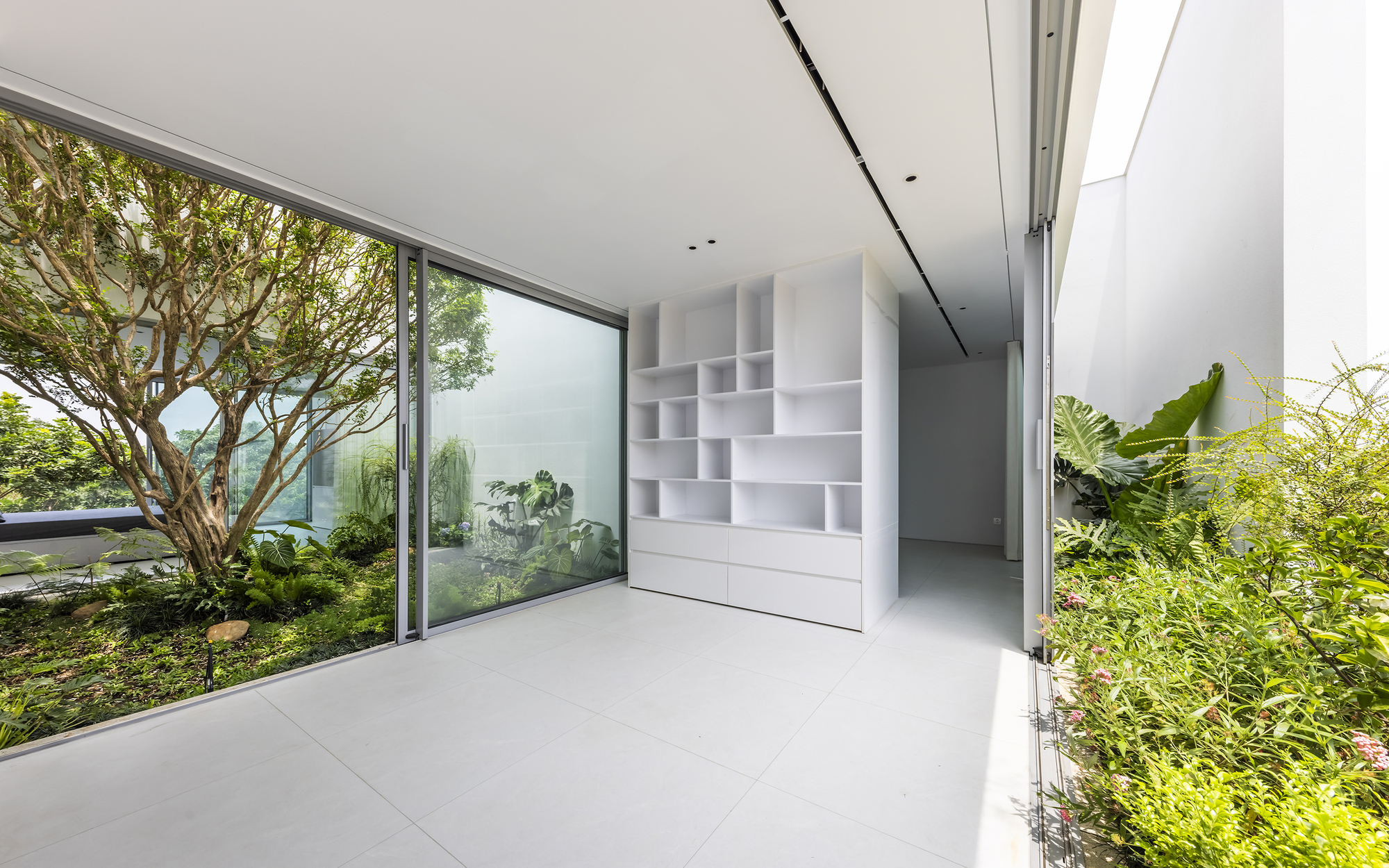 Interior corridor with white modular shelving and full-height glazing framing a planted courtyard
