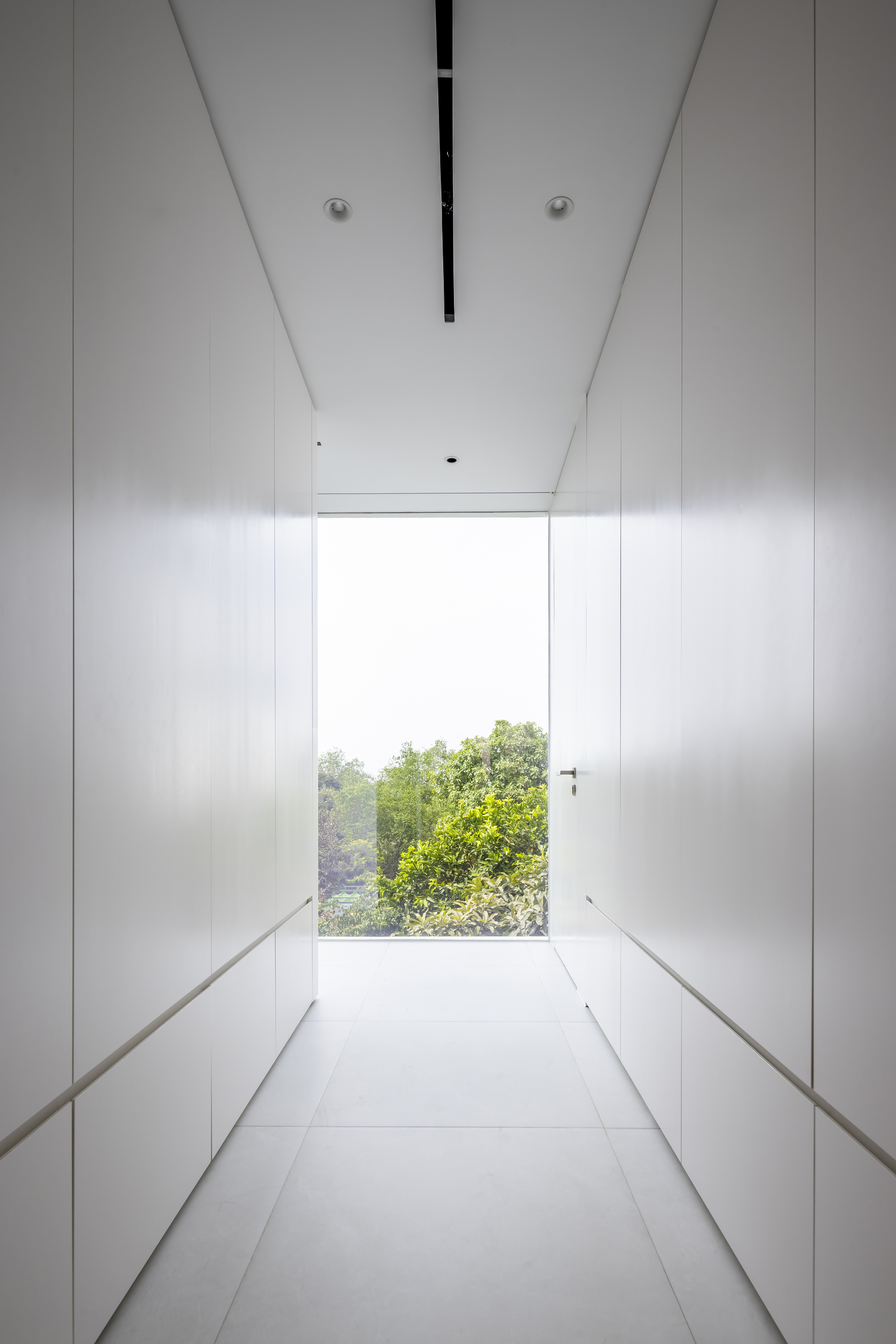 White corridor with full-height storage cabinetry terminating at a window framing treetops
