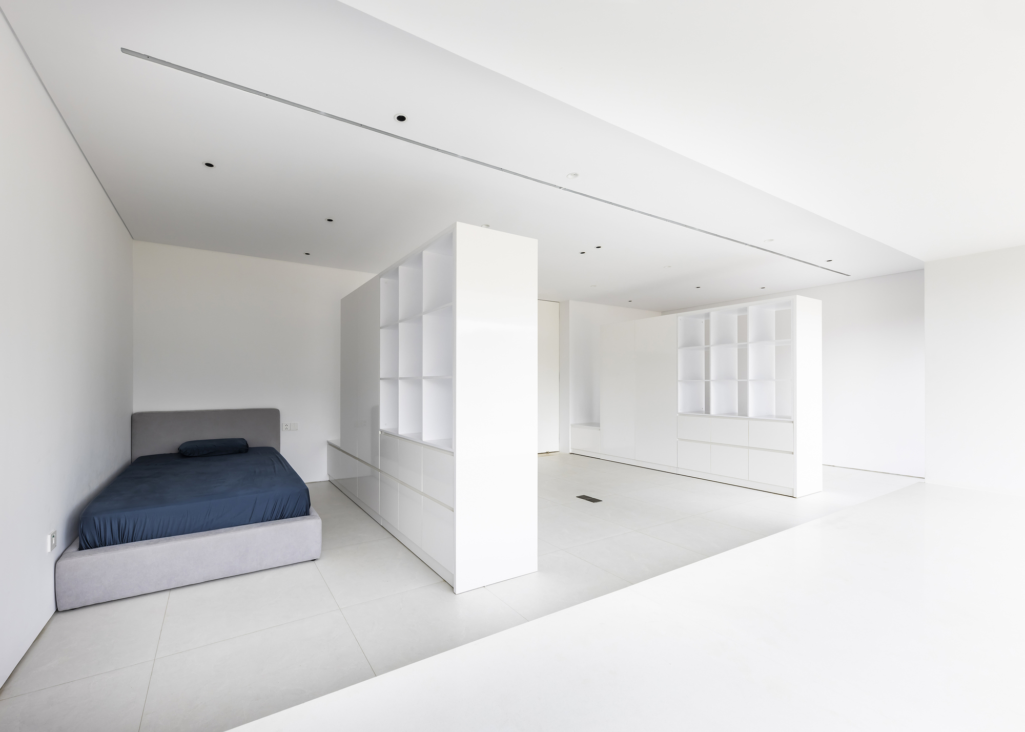 Open-plan bedroom alcove with bed and freestanding white partition wall dividing space from adjacent storage area