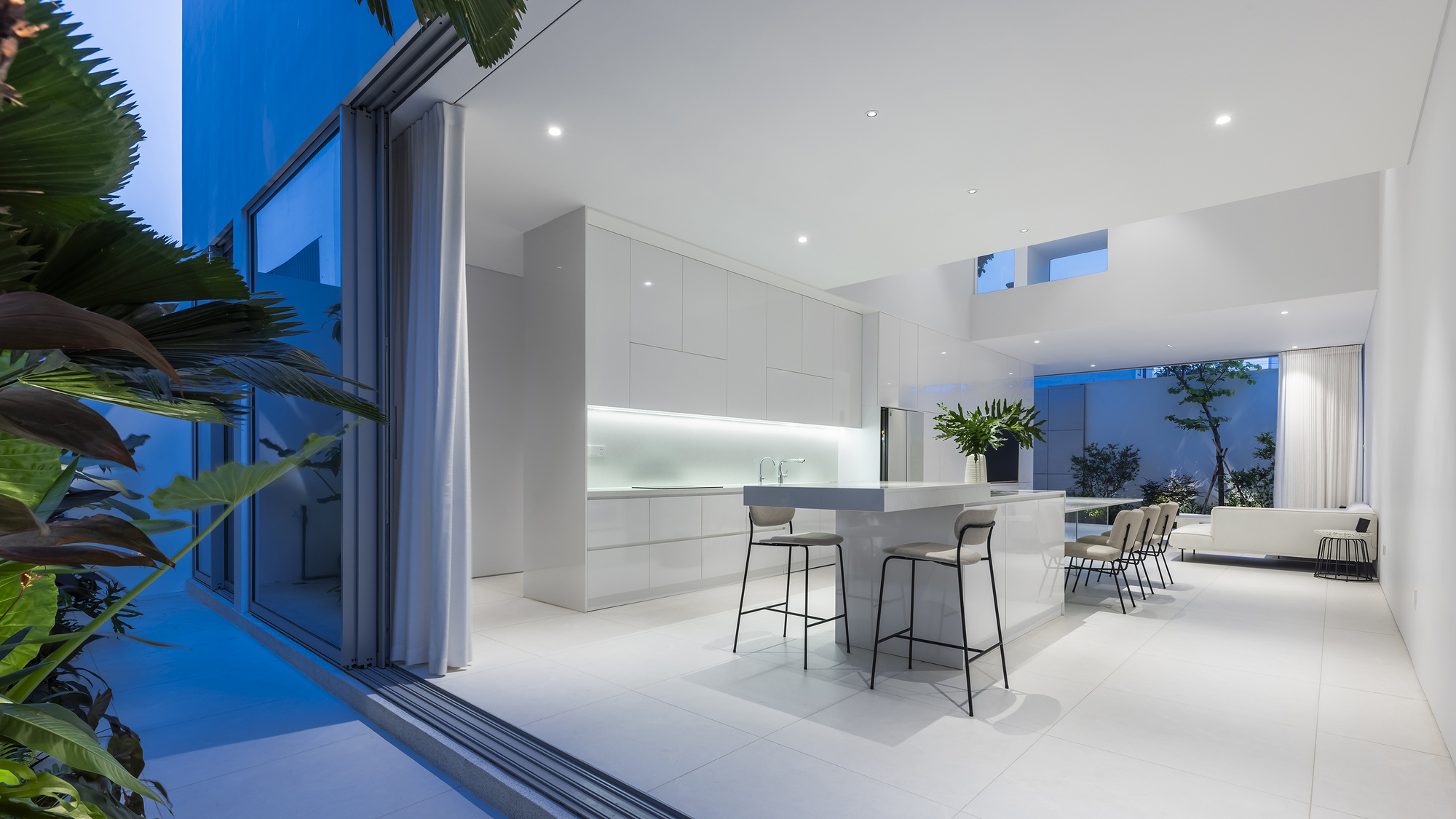 Open kitchen and dining area at dusk with bar stools and sliding glass doors framing tropical plants