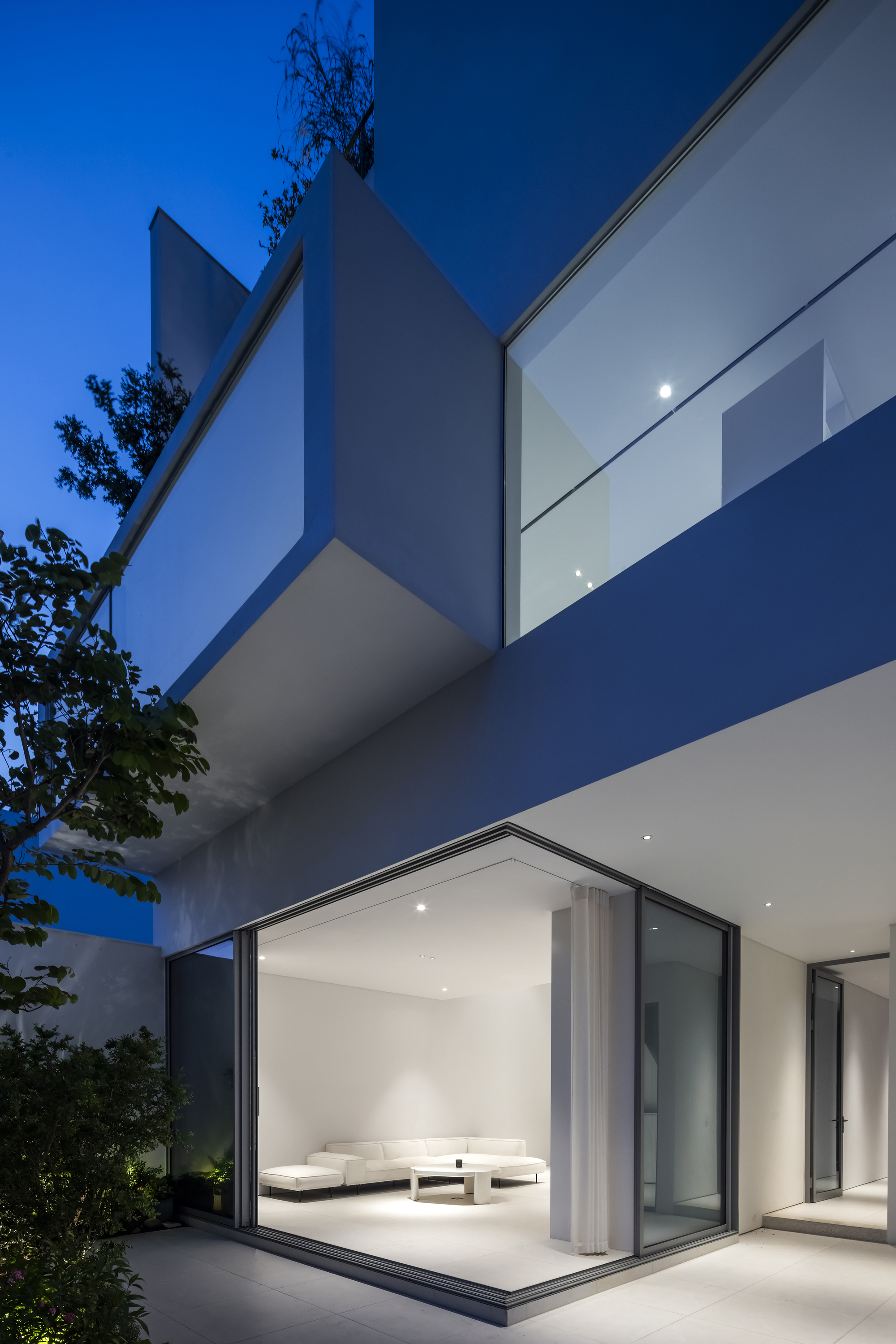 Stacked cantilevered volumes with floor-to-ceiling glass and white rendered walls at blue hour
