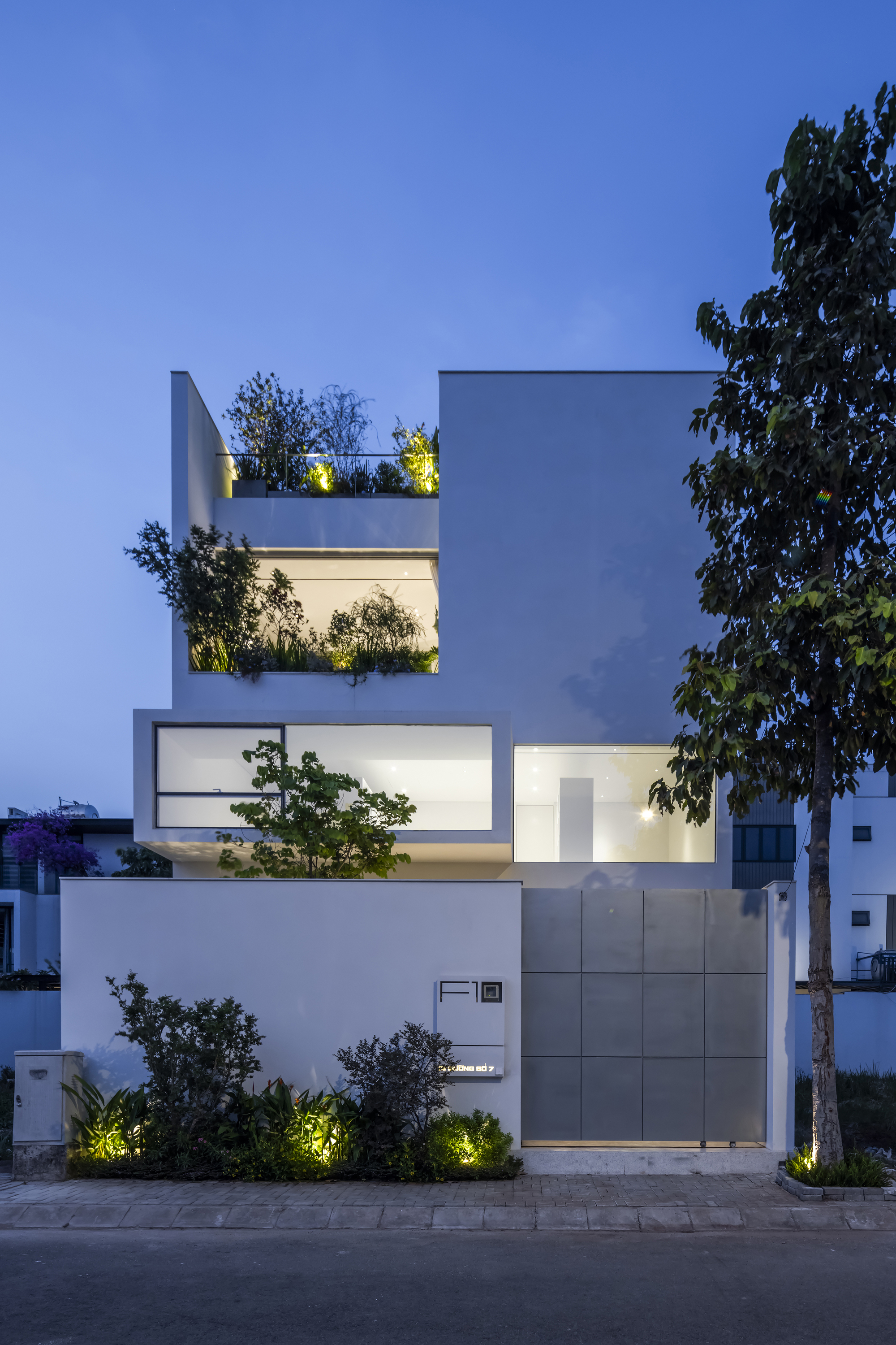 Street facade at dusk showing stacked volumes with planted terraces and uplighted vegetation